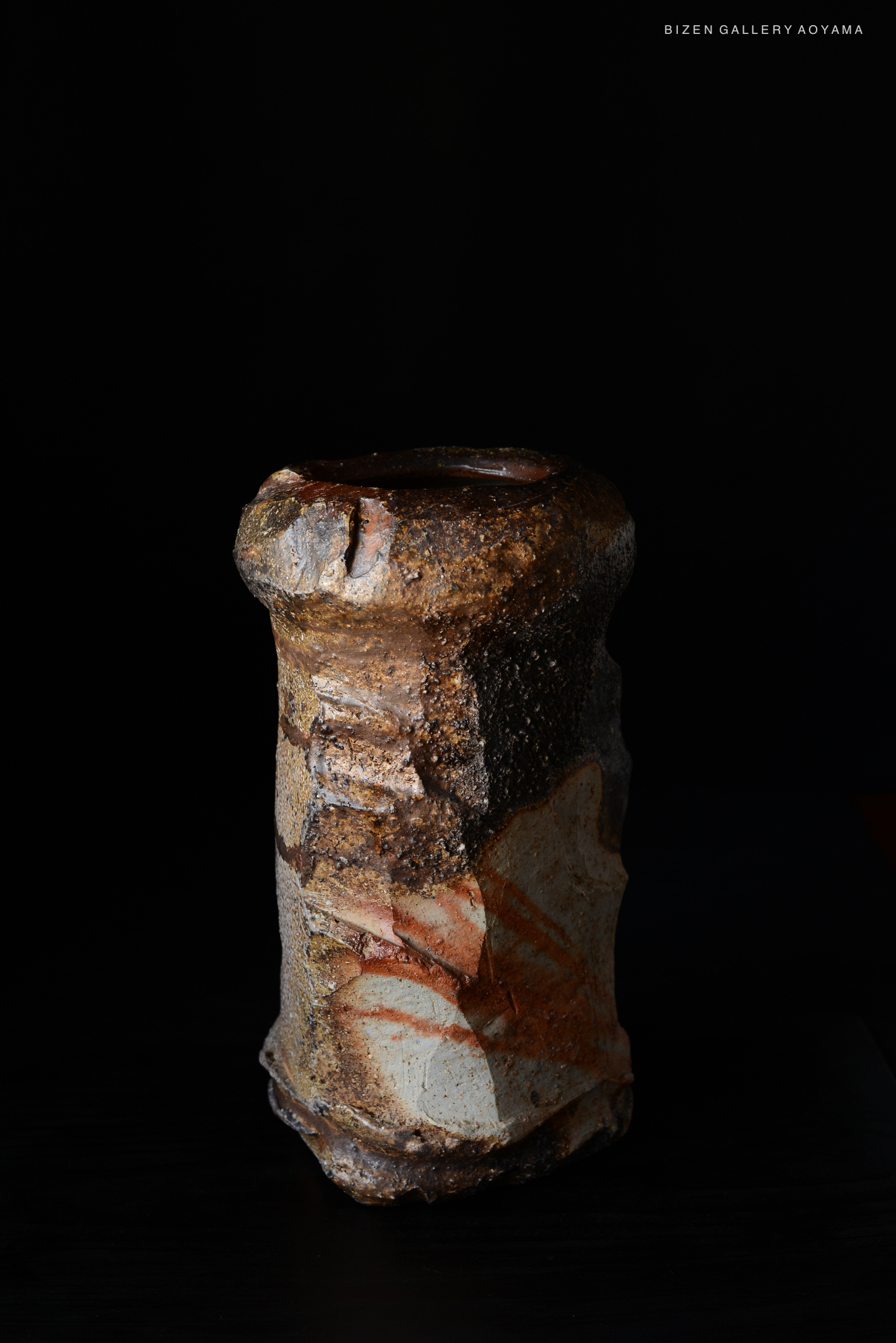 A unique ceramic vase with a textured surface and earthy colors, set against a black backdrop.