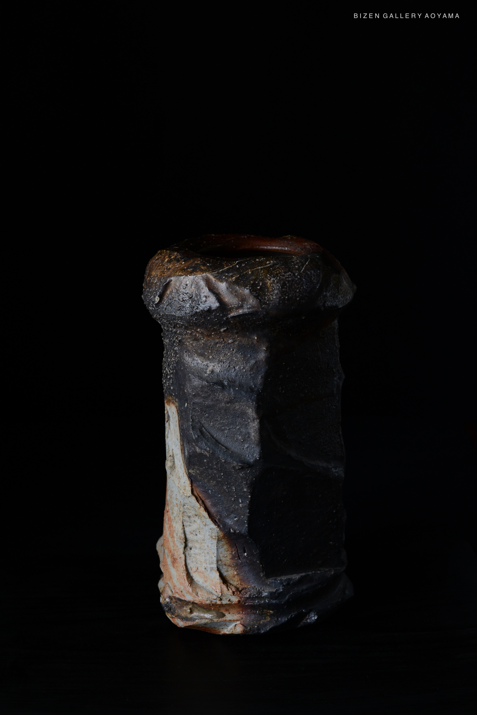 A dark ceramic piece with a textured surface, showcasing a unique shape, placed against a black background.