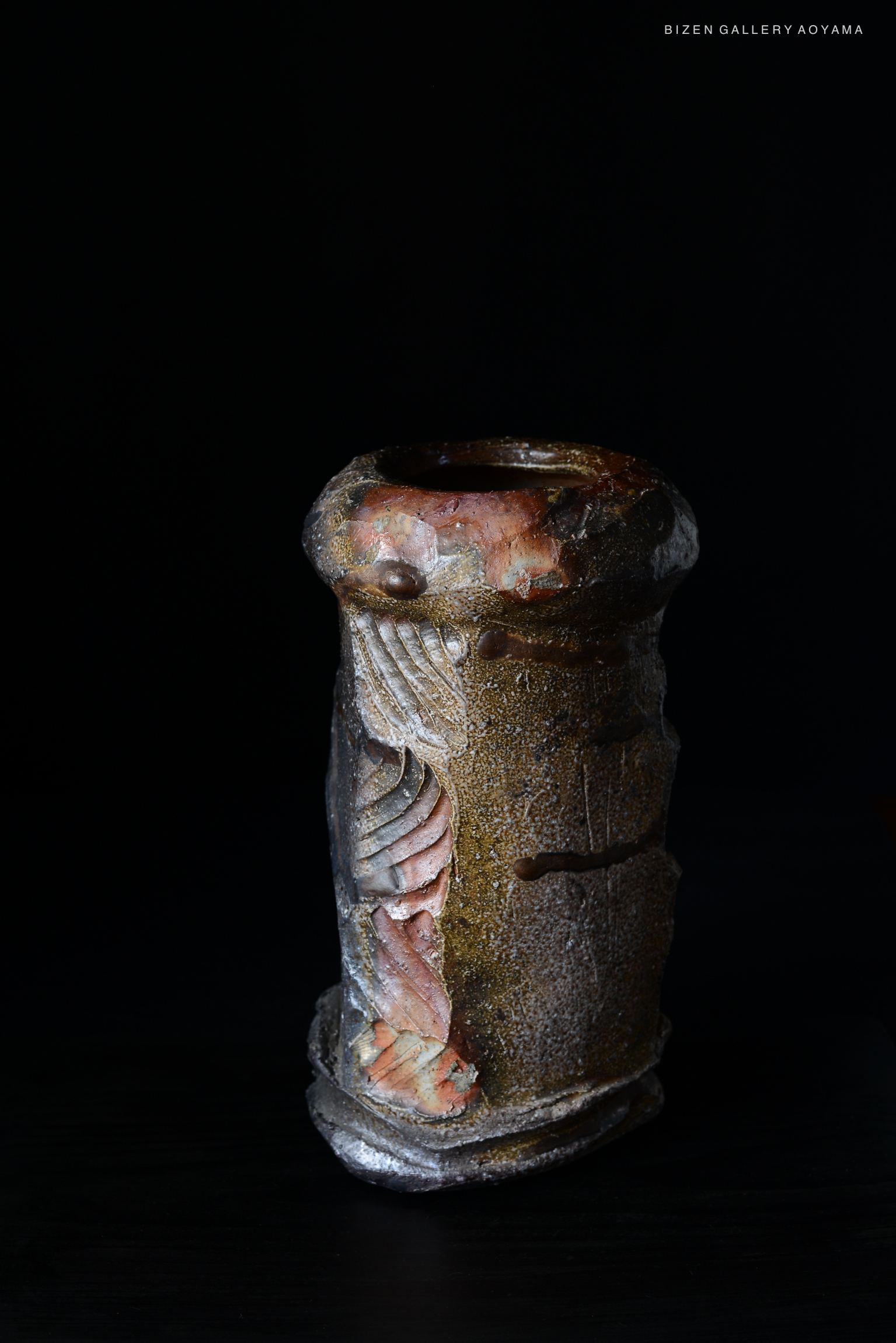 A handcrafted ceramic tsubo showcasing intricate carvings and a textured surface, displayed against a dark background.