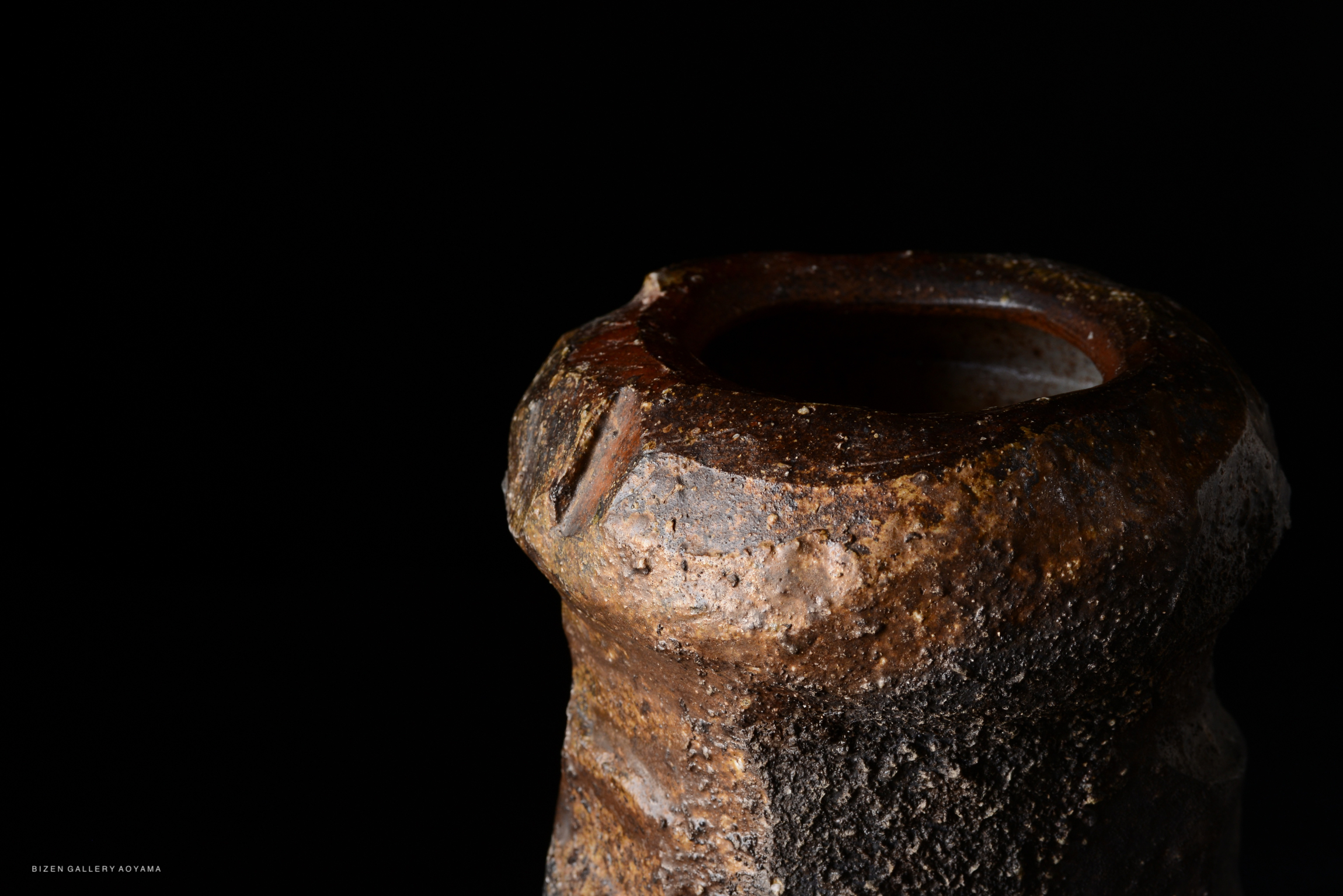Close-up of a ceramic tsubo by Kenji Matsushima, featuring a textured surface and earthy colors, set against a black background.