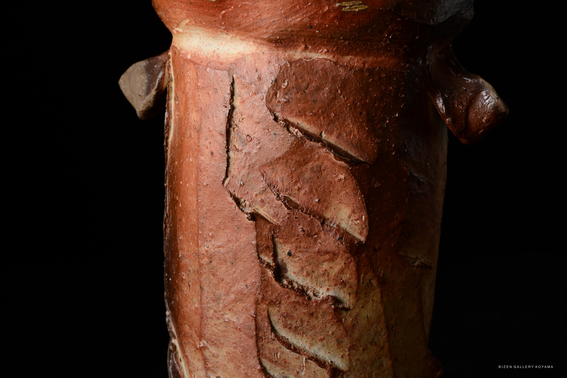Close-up view of a ceramic vessel showcasing intricate textured surface details and a rich, earthy glaze.