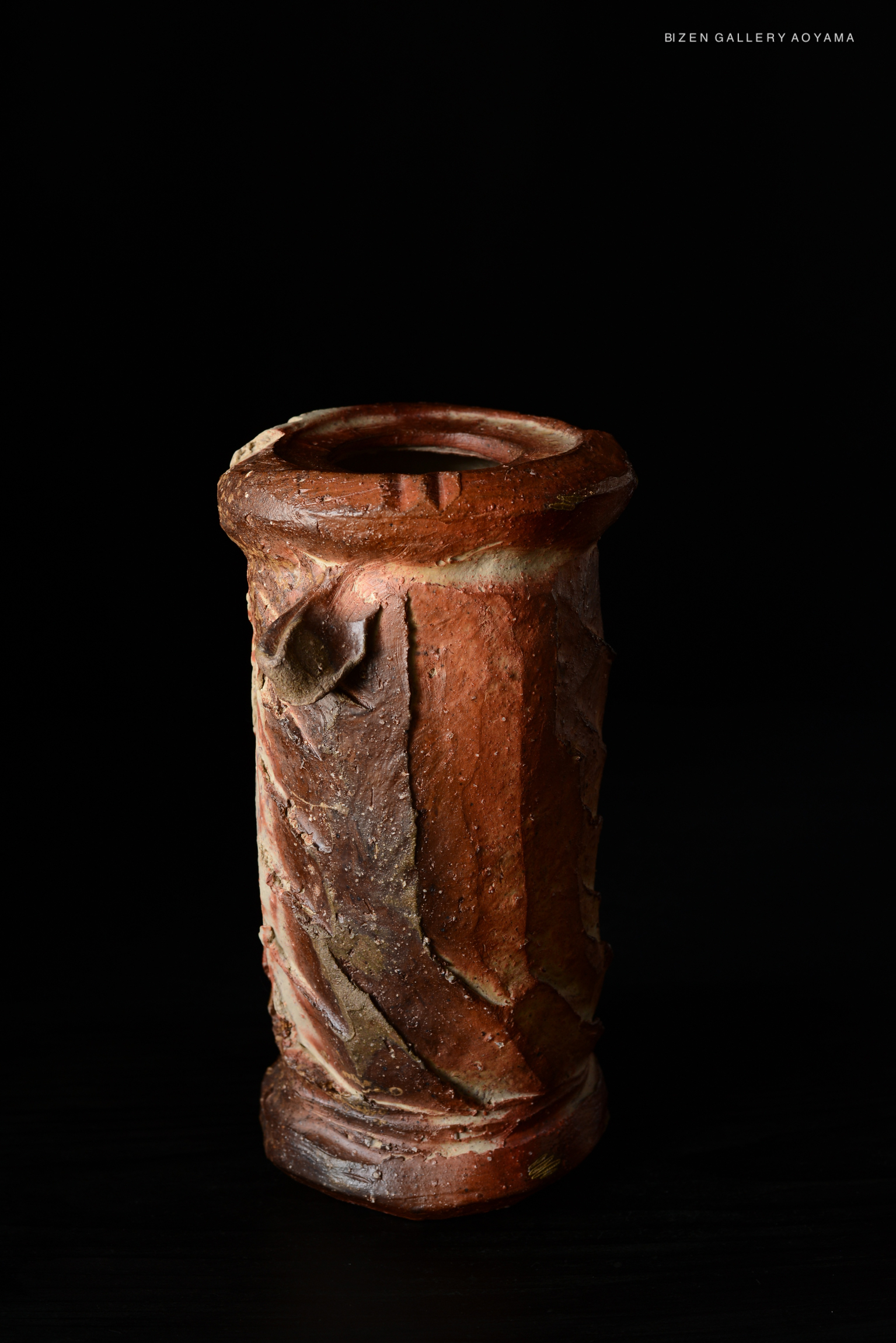 A close-up of a ceramic vase with a textured surface, showcasing earthy tones and unique patterns, set against a dark background.