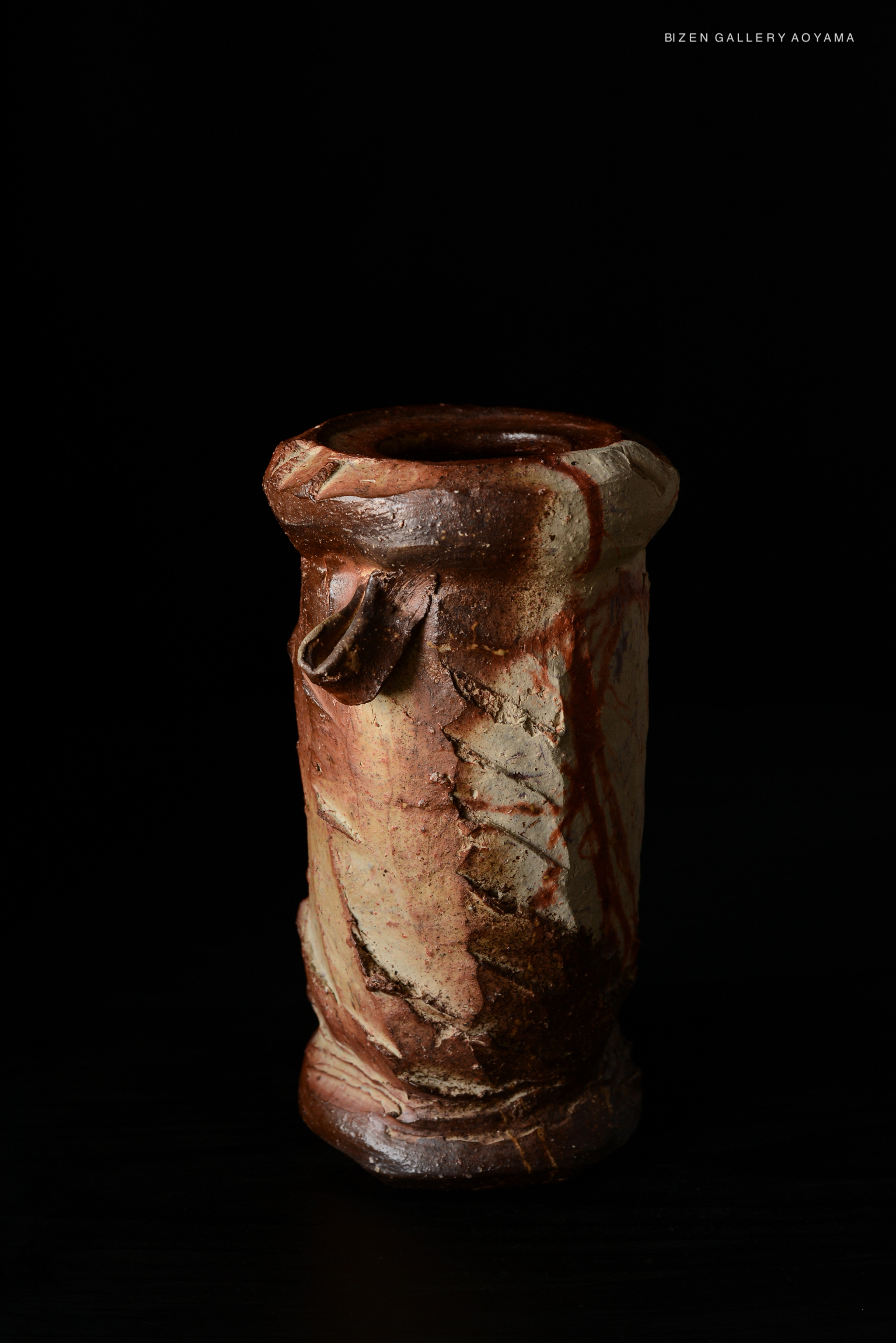 A ceramic vessel with a textured surface, featuring earthy tones and a decorative rim, set against a dark background.