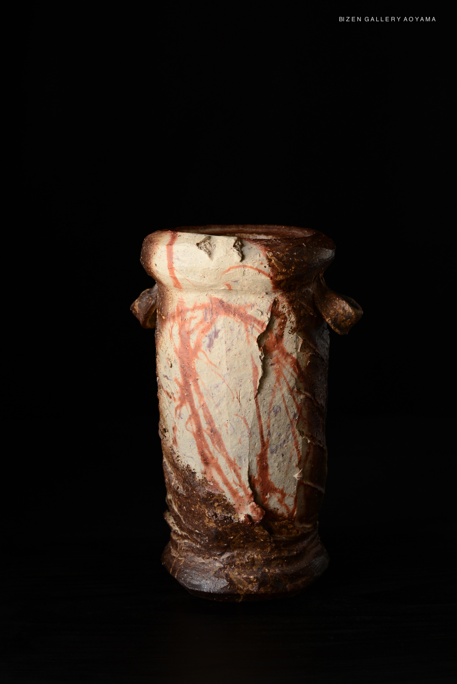 A ceramic vase by Kenji Matsushima, featuring a textured surface with red markings, displayed against a black background.