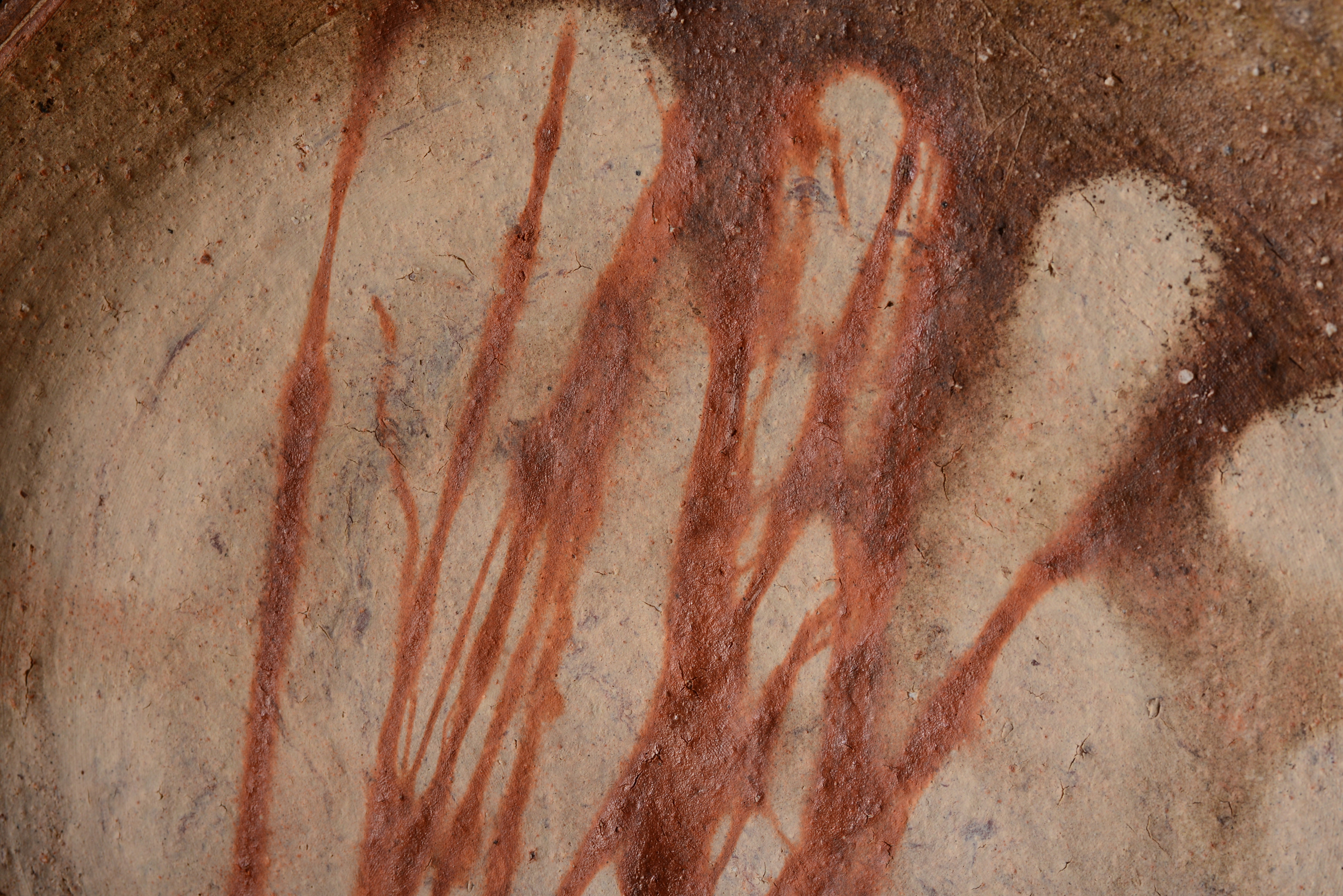 Close-up of a ceramic surface featuring earthy tones and streaks of reddish-brown glaze.