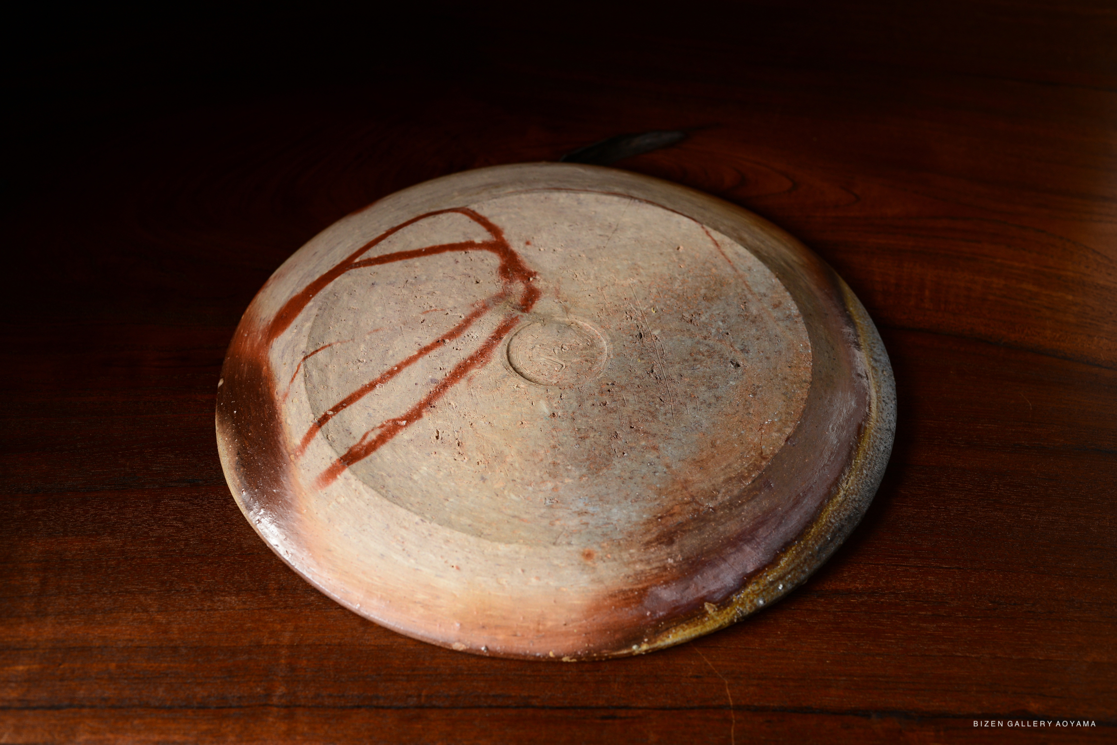 A close-up view of a ceramic plate featuring earthy tones and a subtle decorative line pattern, resting on a wooden surface.