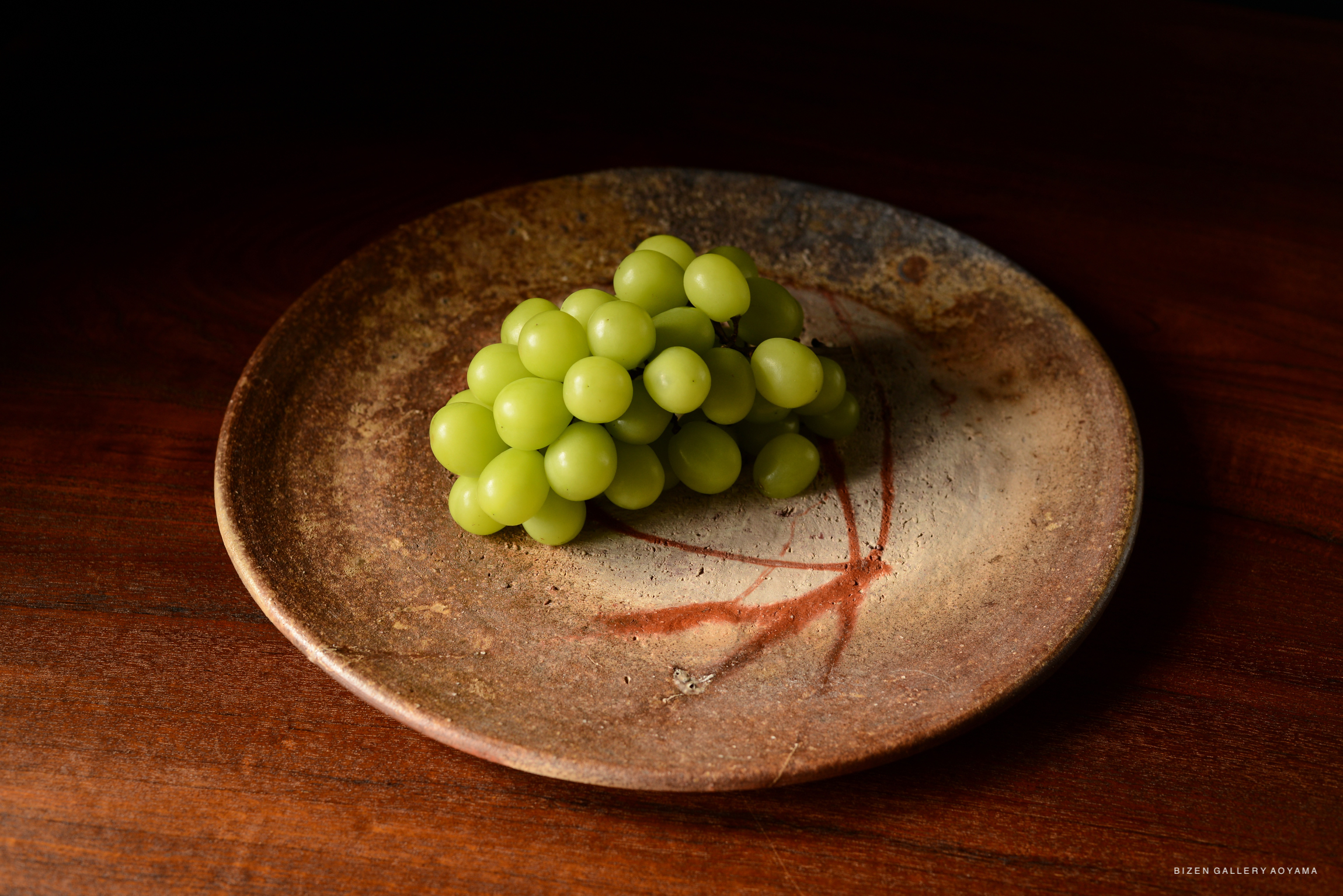 A cluster of green grapes arranged on a rustic ceramic plate with a textured surface and a subtle reddish design.