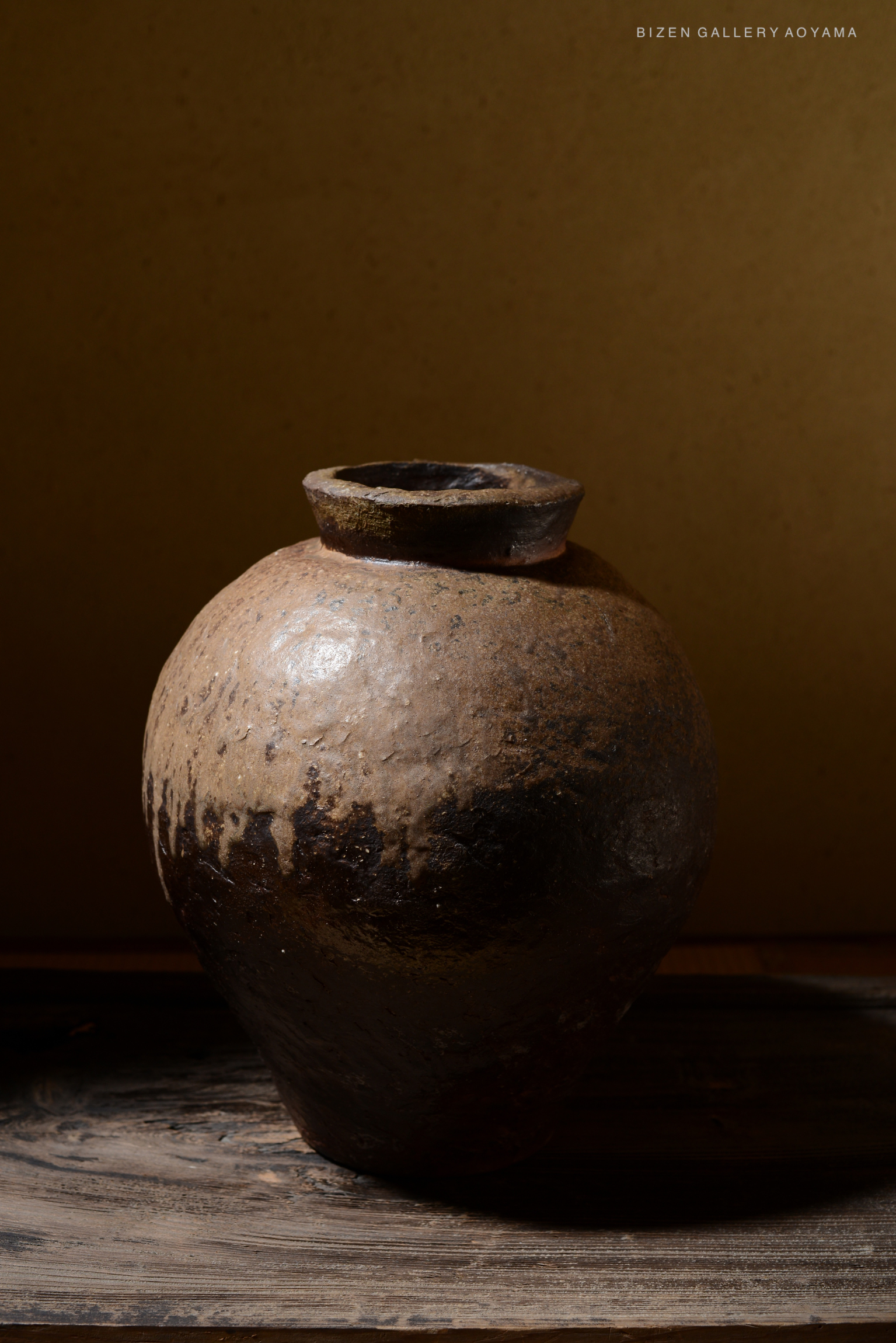 A rustic ceramic tsubo with a textured surface, displayed on a wooden surface, against a neutral background.