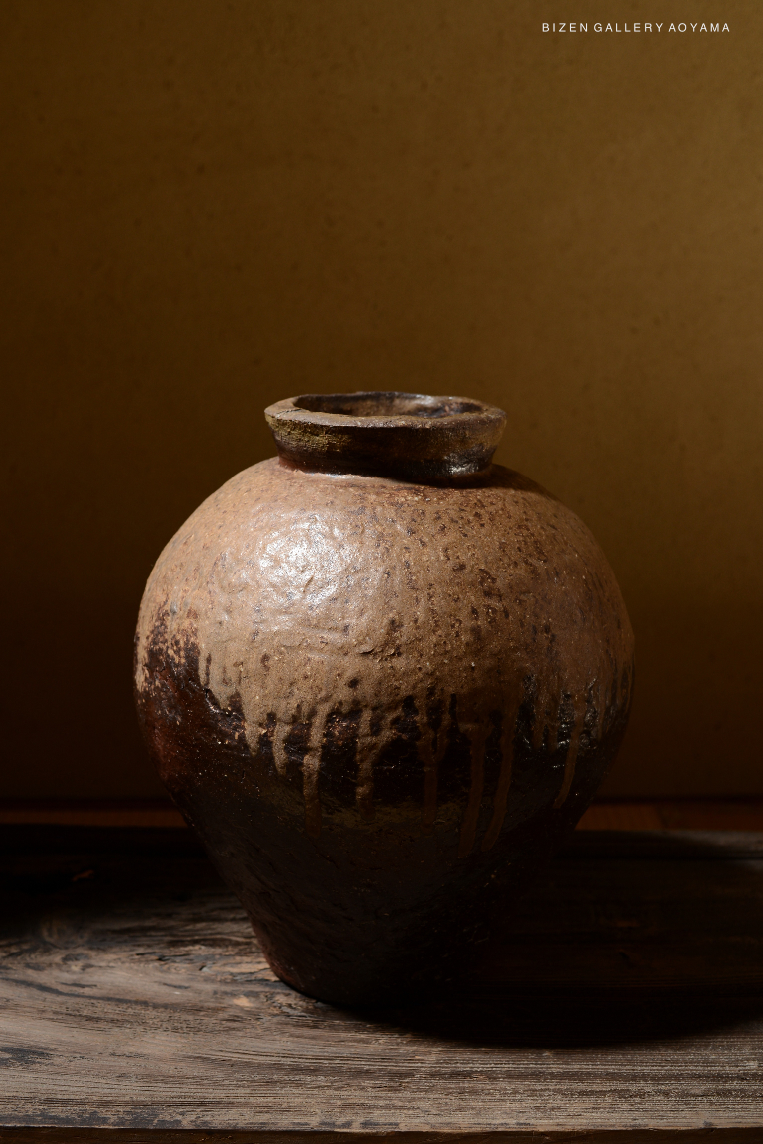 A large ceramic tsubo with a brown and dark glaze, featuring a round body and a slightly flared neck, displayed on a wooden surface.