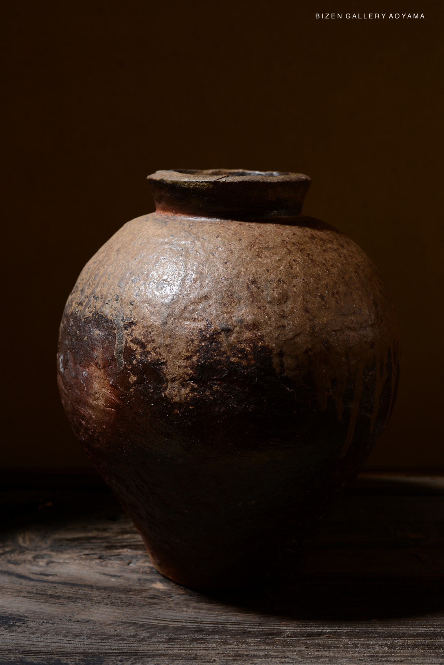 A close-up of a Bizen pottery tsubo displayed against a dark background, showcasing its unique texture and earthy colors.
