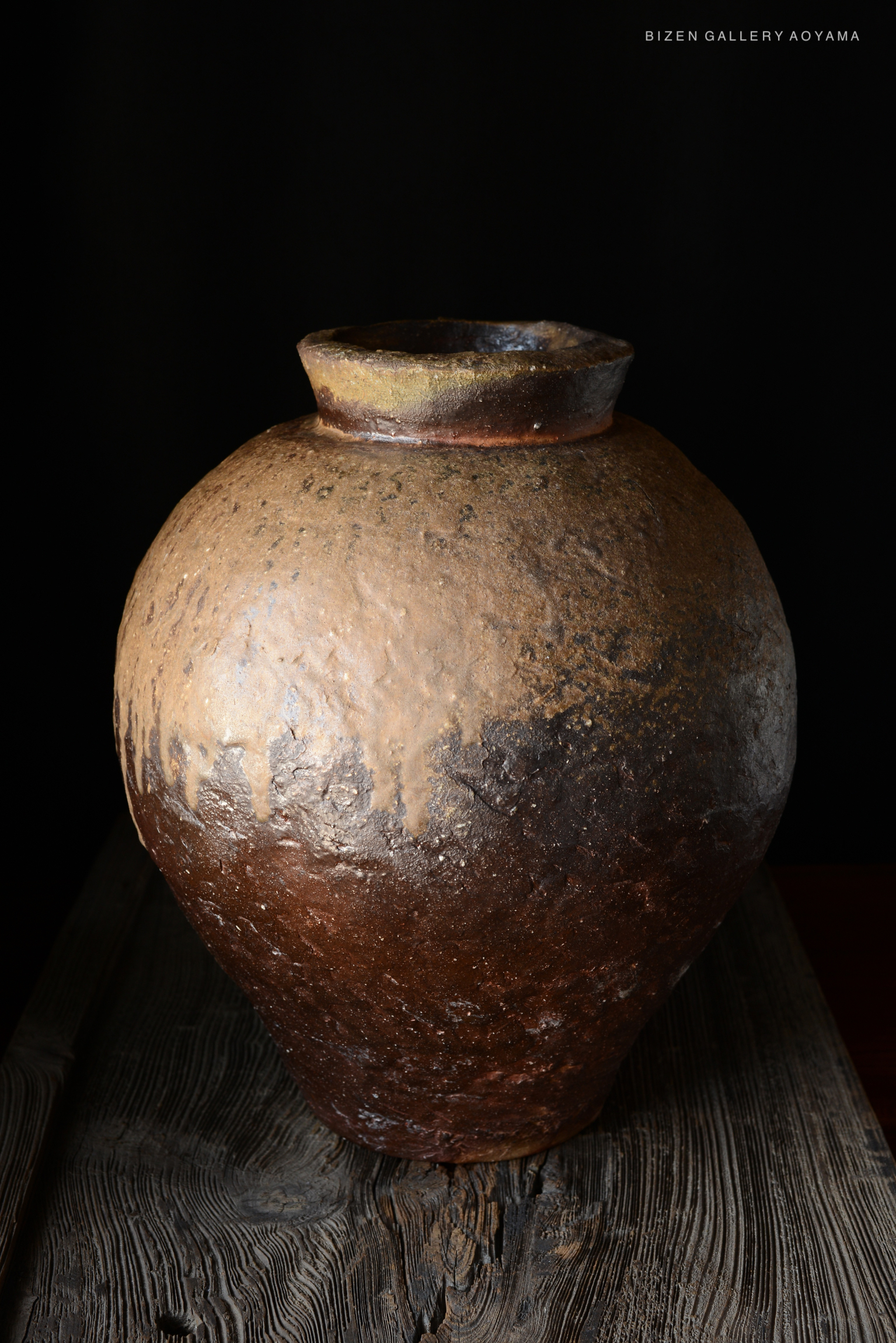 A traditional Bizen pottery tsubo with a rounded shape and textured surface, displayed on a wooden surface against a dark background.