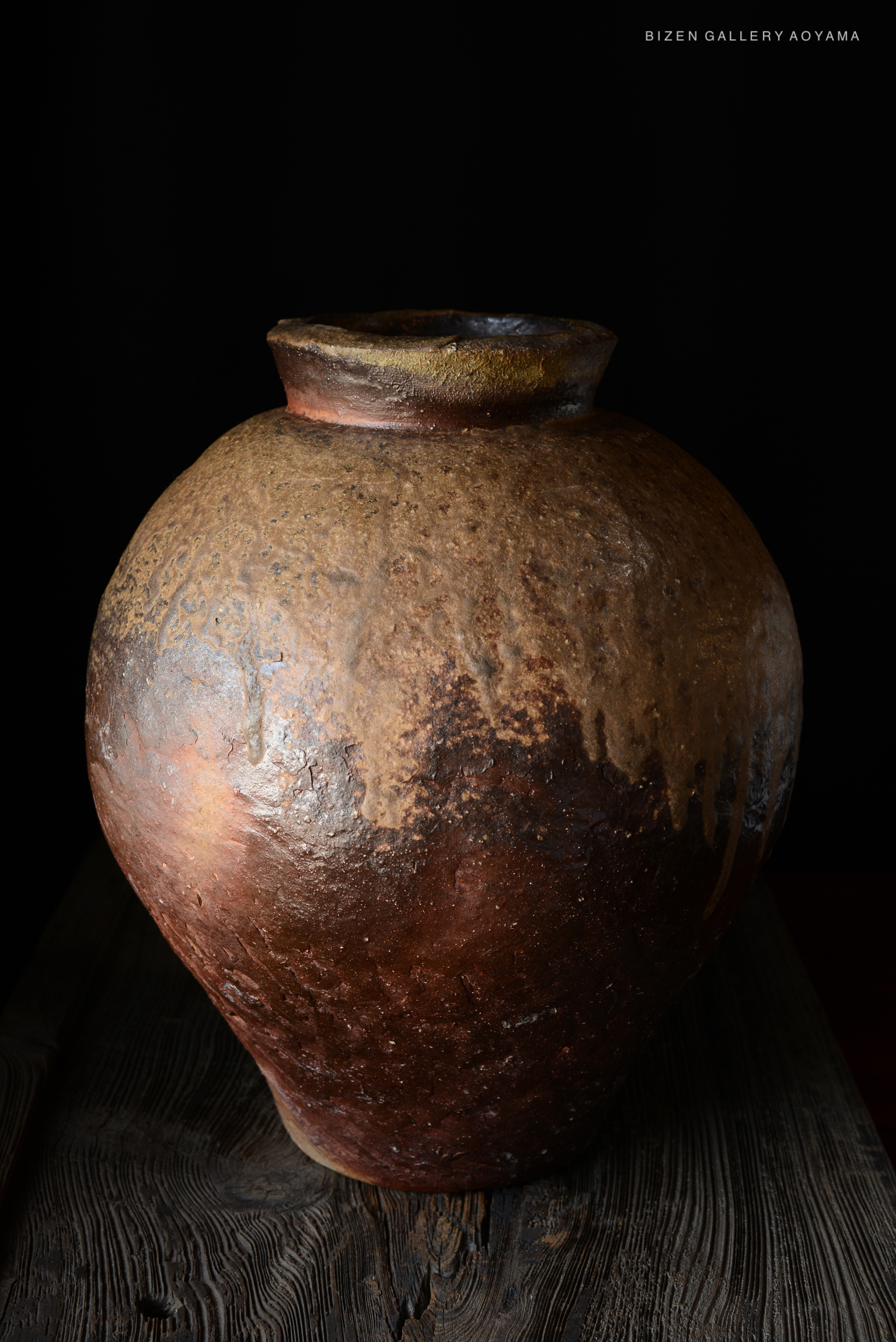 A large, round Bizen pottery tsubo with a textured surface, showcasing earthy tones of brown and hints of orange, set against a dark background.