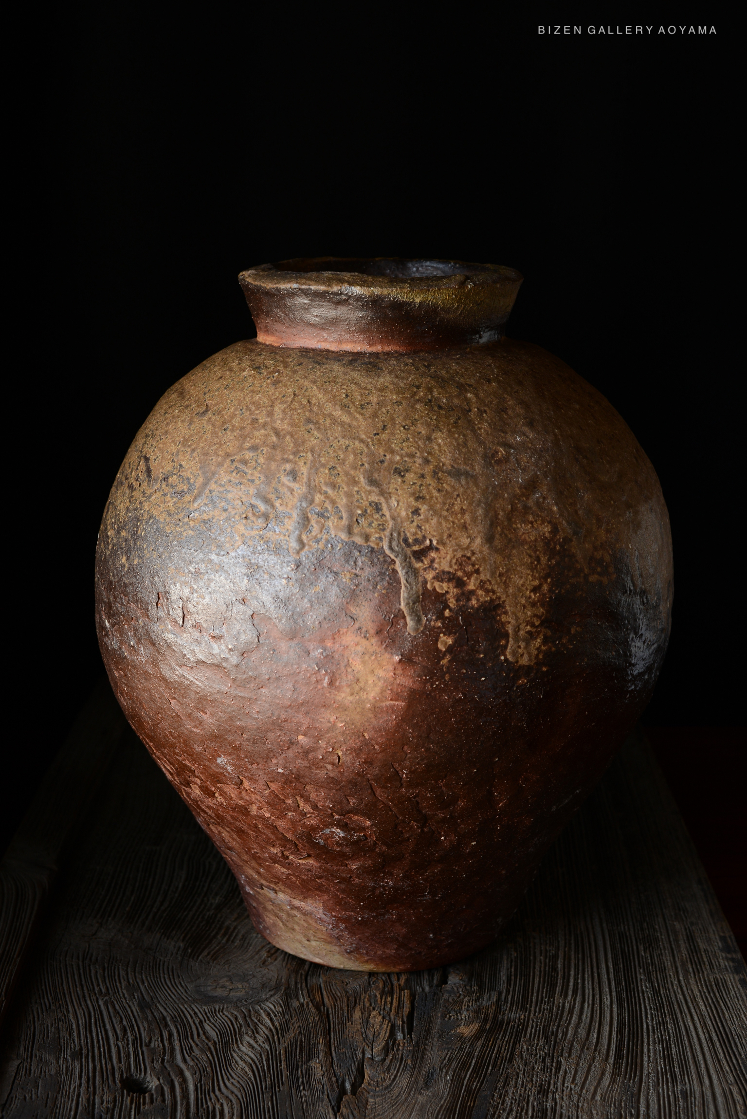 A large, rustic Bizen ceramic tsubo vase with textured surface and earthy tones, set against a dark background.