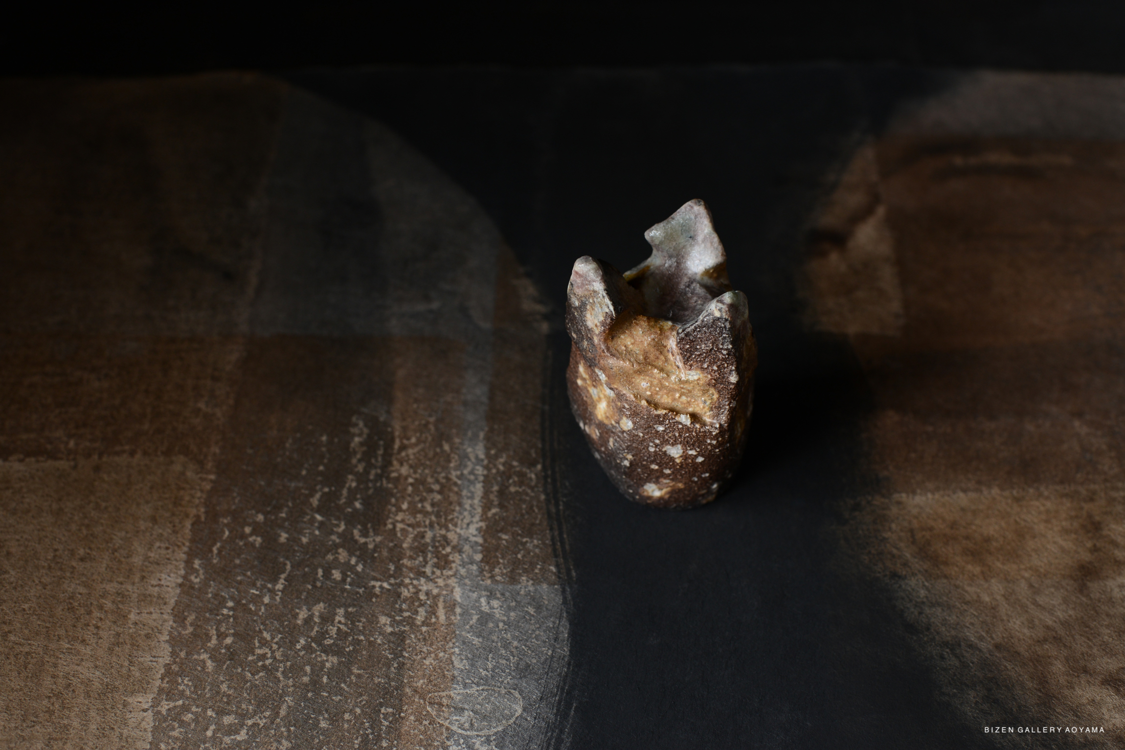 A close-up image of a unique, textured ceramic piece resting on a dark surface with subtle patterns.