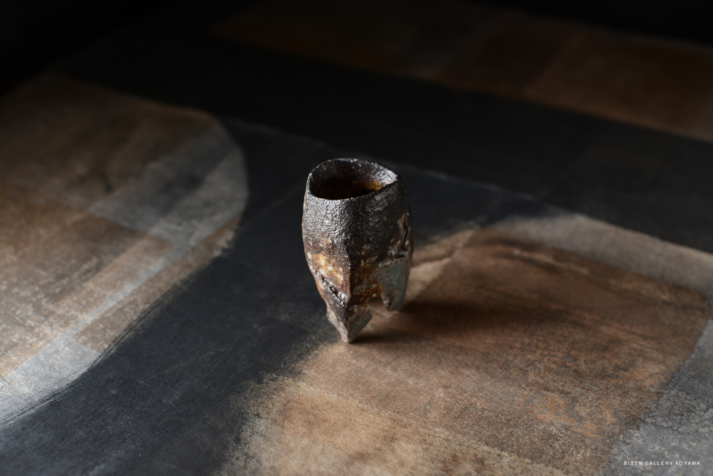 A unique, handcrafted ceramic cup with a textured surface, positioned on a dark, abstract patterned background.