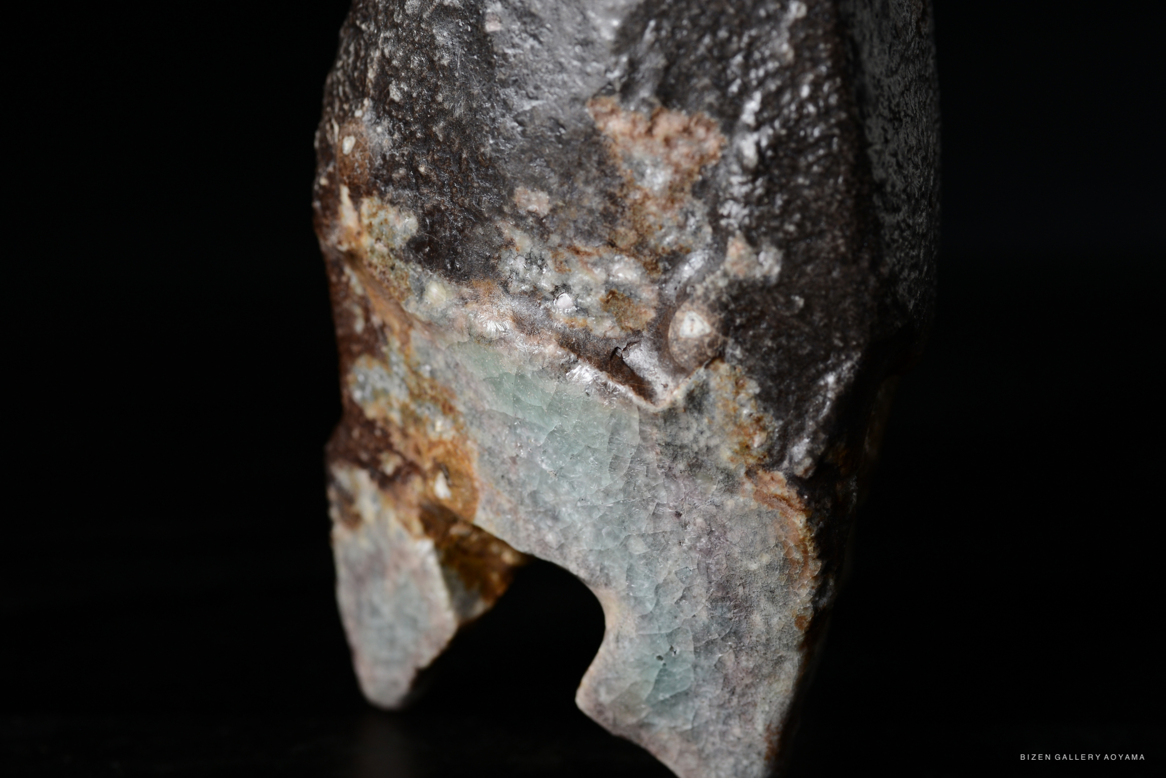 Close-up of a textured stone with a mix of gray, brown, and light blue hues, featuring a jagged edge and irregular shape.