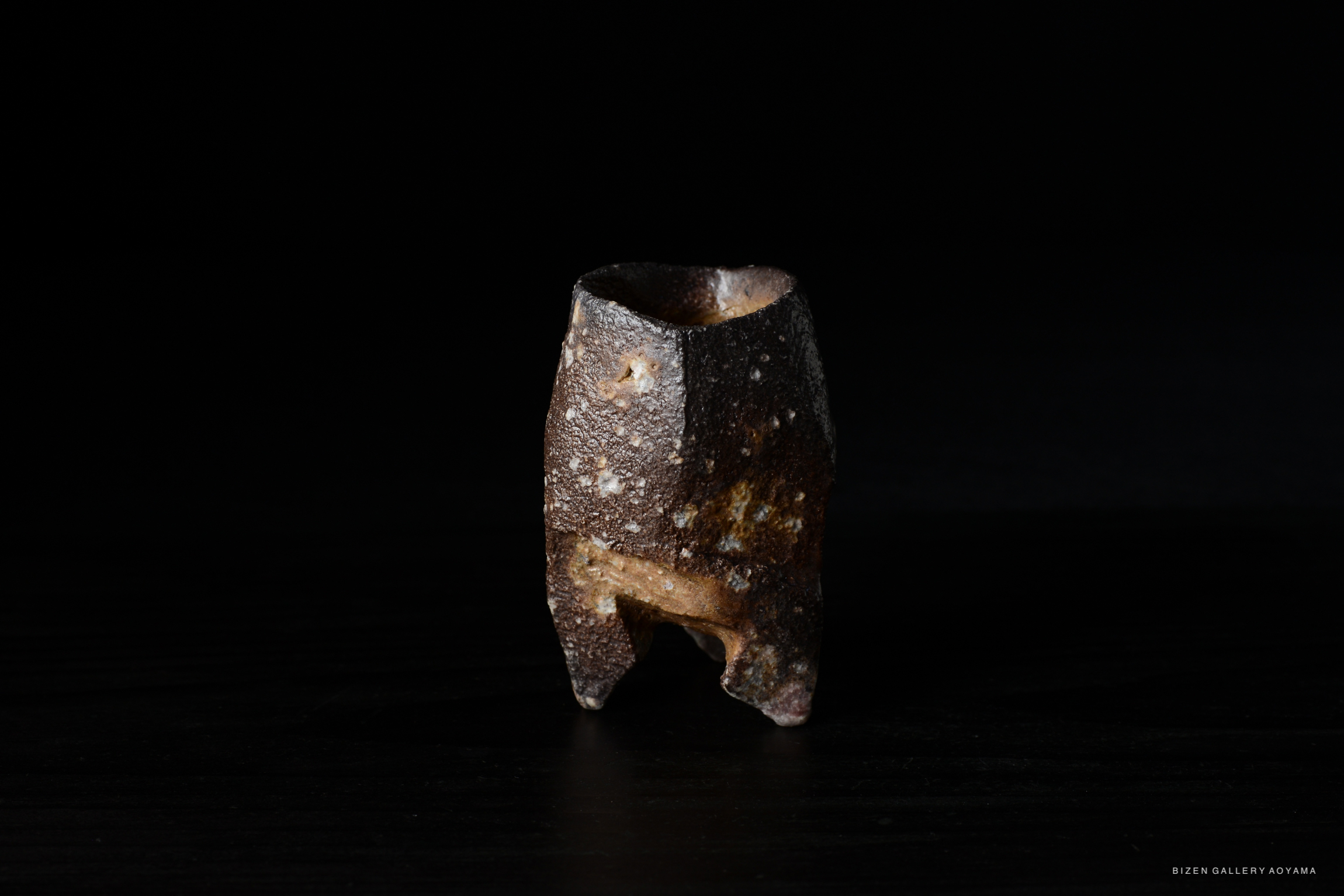 A rustic ceramic vessel with a textured surface, displayed against a dark background.