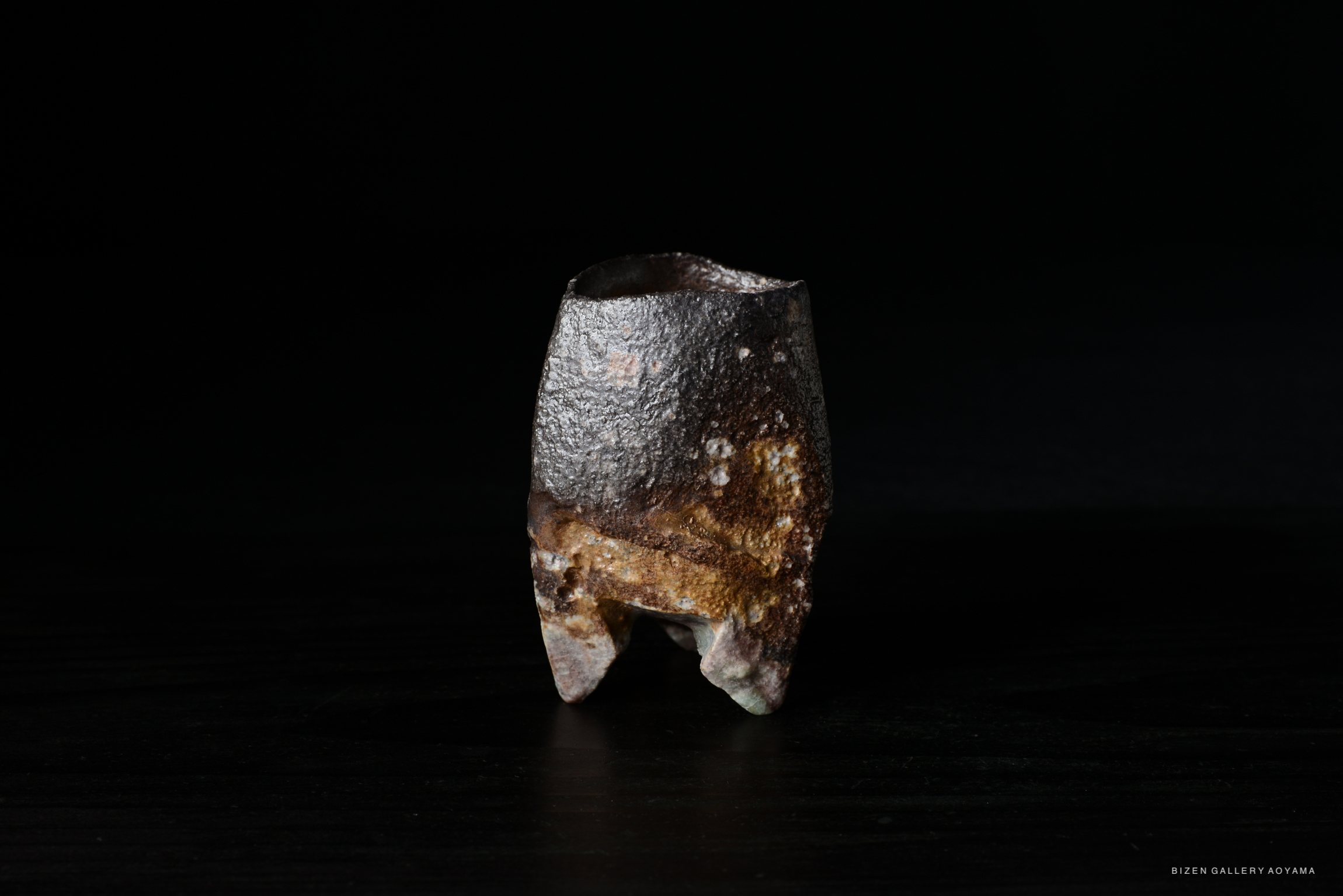 A close-up of a rustic ceramic piece with a textured surface, displayed against a dark background.