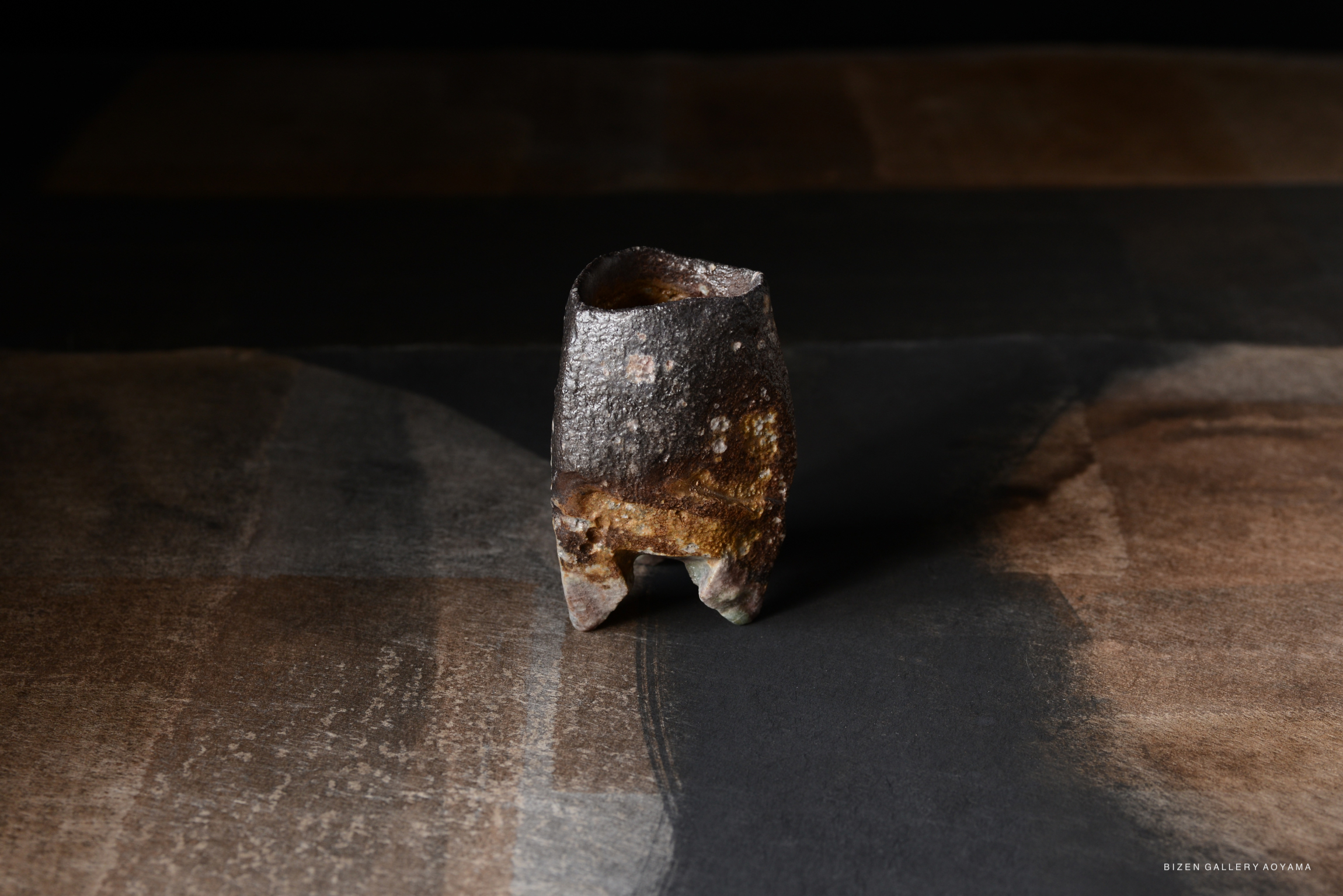 A textured ceramic object with a rustic finish, placed on a dark surface showcasing various shades of brown.