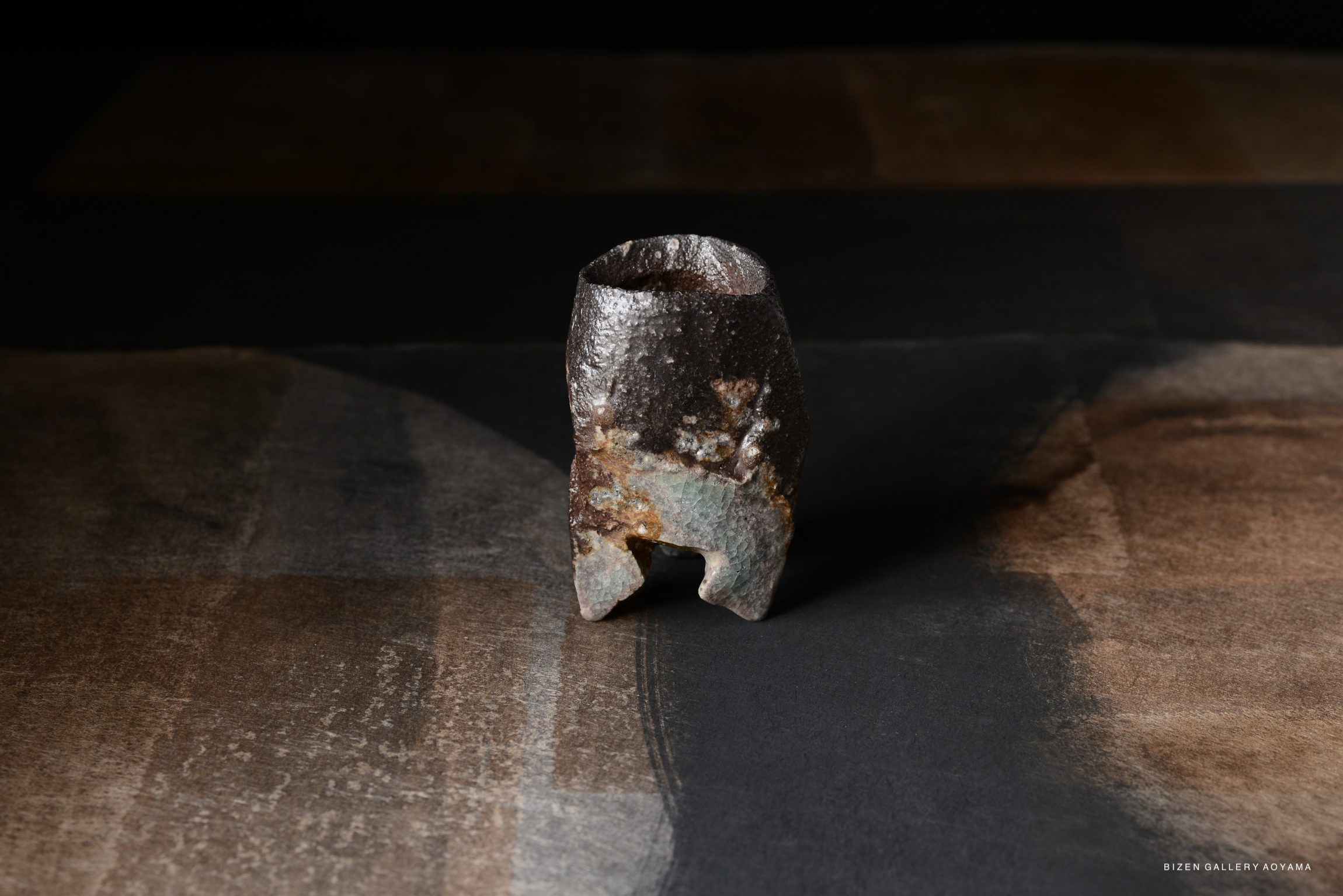 A close-up of a unique Bizen pottery piece, displaying earthy tones and a textured surface on a dark background.