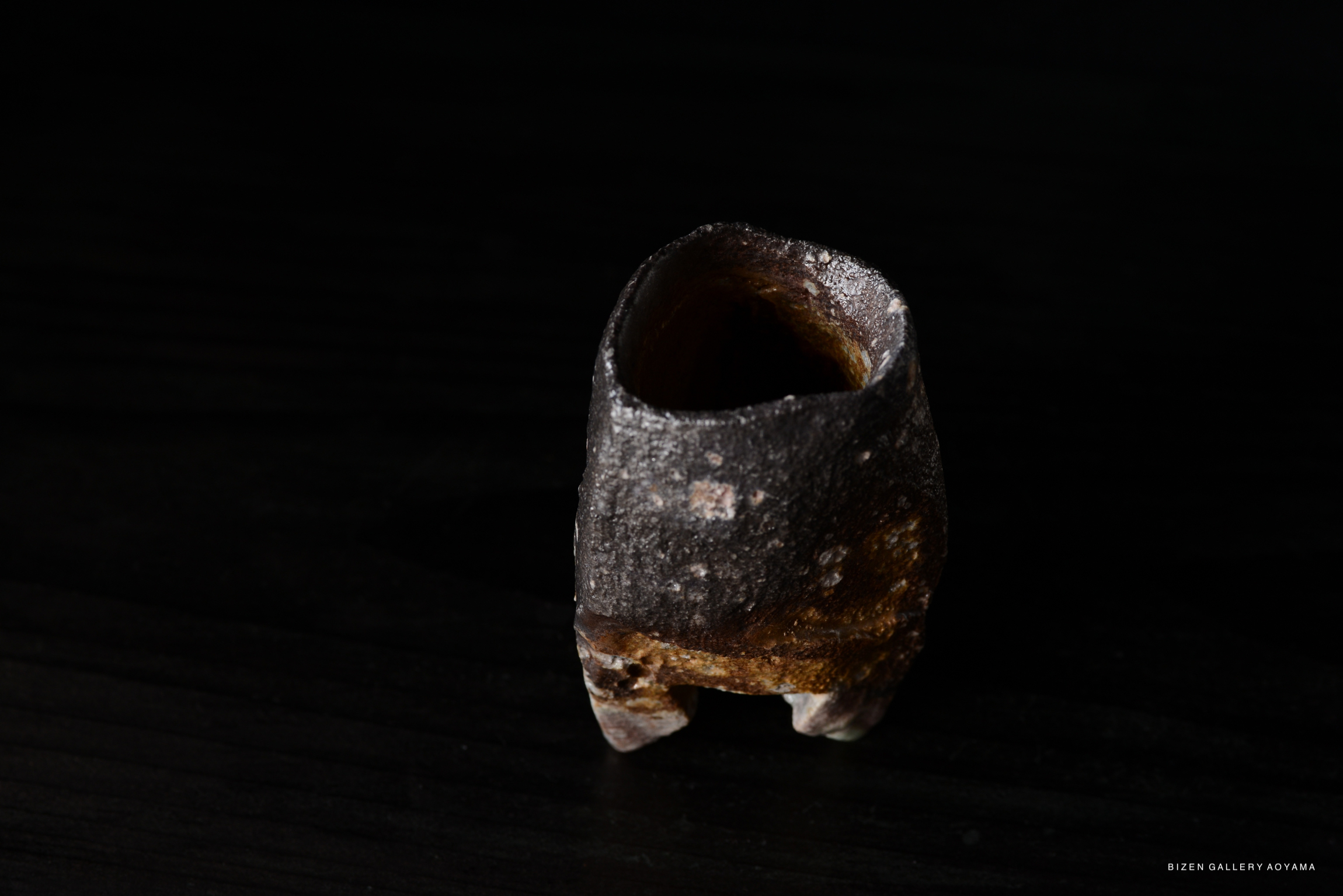 A unique, textured ceramic vase with a dark, earthy tone, placed on a black wooden surface.