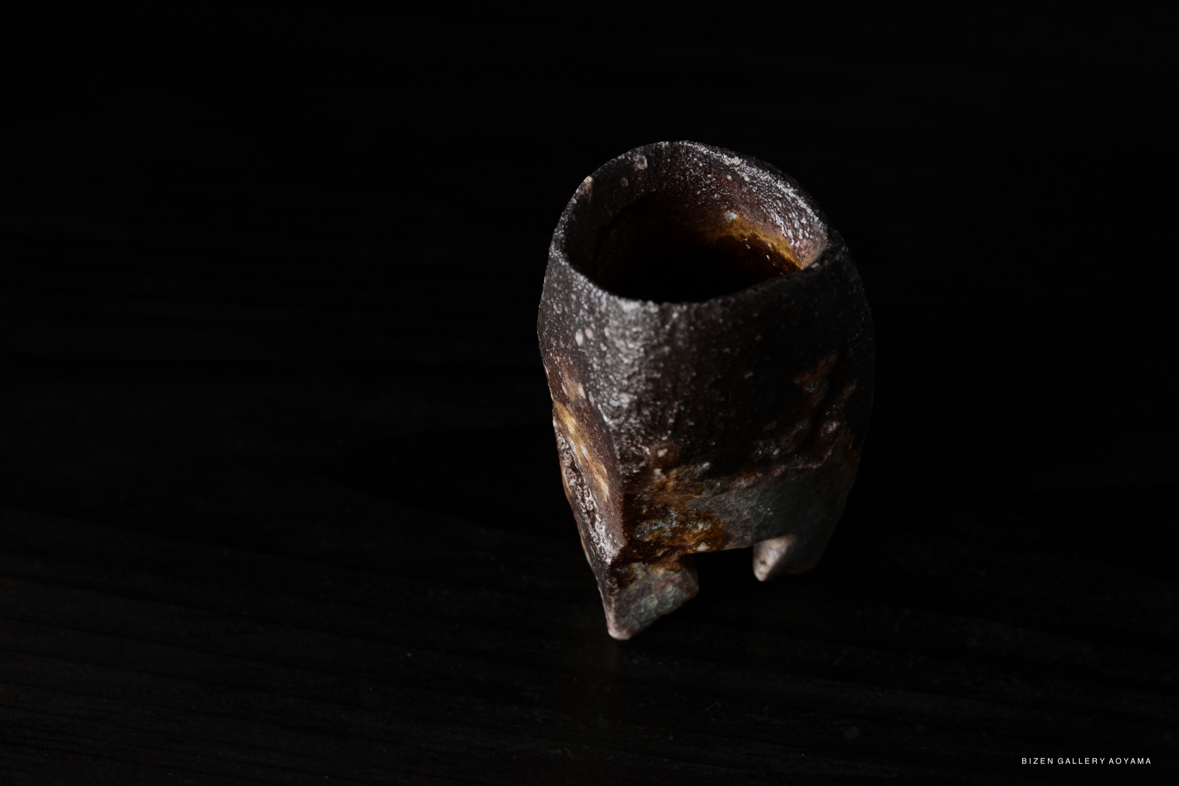 Close-up of a textured ceramic vessel with a dark finish, placed on a black surface.