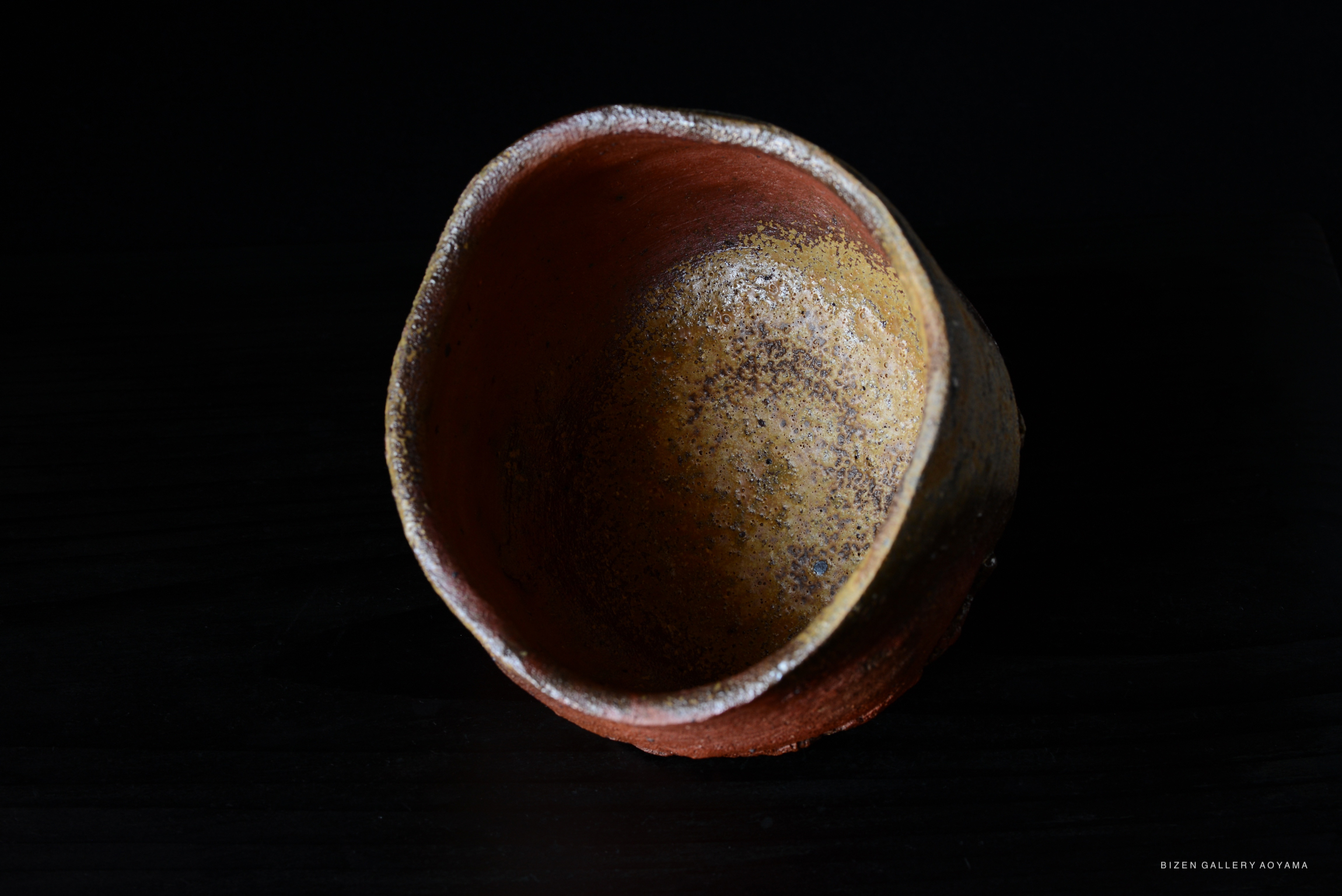 A close-up view of a Bizen pottery tea bowl featuring earthy tones and a textured interior, set against a dark background.