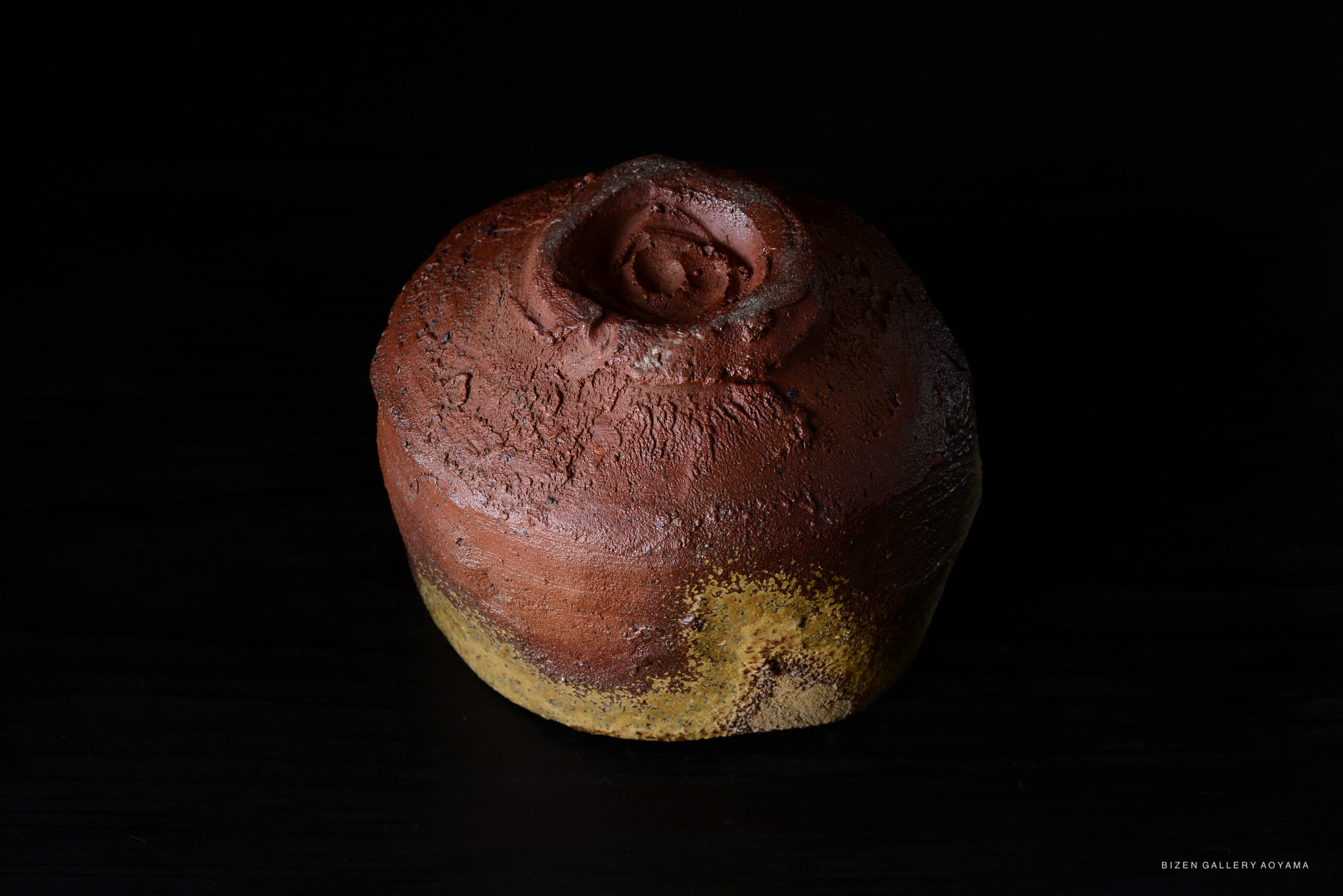 A close-up view of a Bizen tea bowl, showcasing its rich earthy tones and unique textures against a dark background.