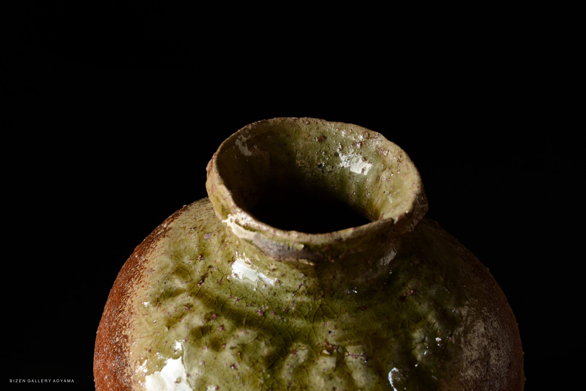 Close-up of a ceramic vase with a green glaze and rough texture, set against a black background.