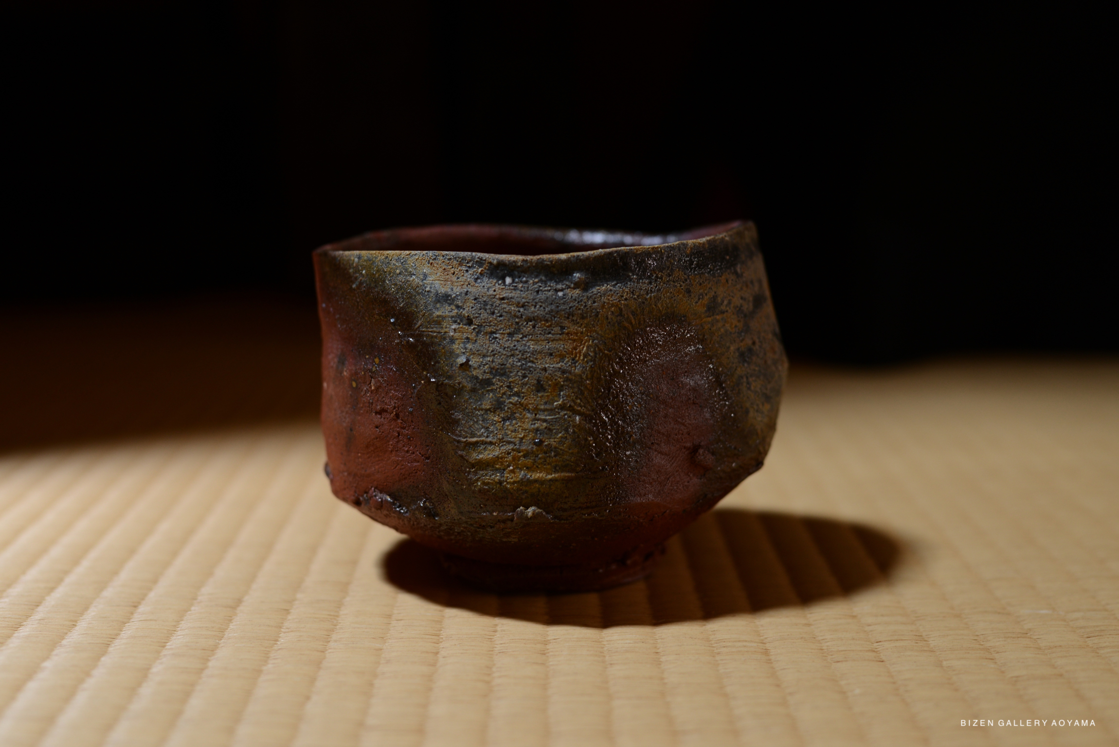 A Bizen teacup placed on a tatami mat, showcasing a dynamic design with earthy tones and textures, under soft lighting.