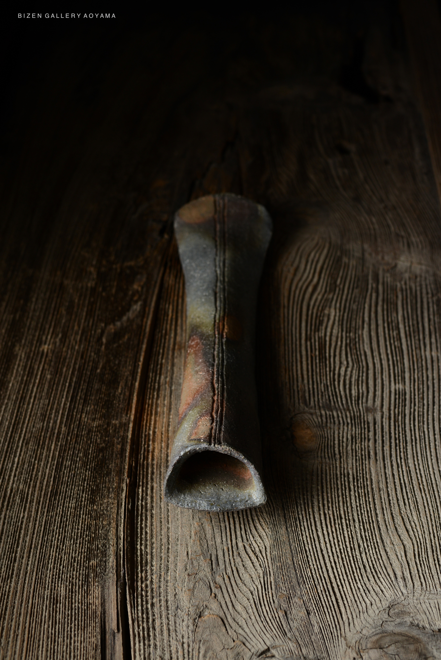 A close-up view of a unique, handcrafted pottery piece resting on a wooden surface, showcasing its intricate texture and colors.