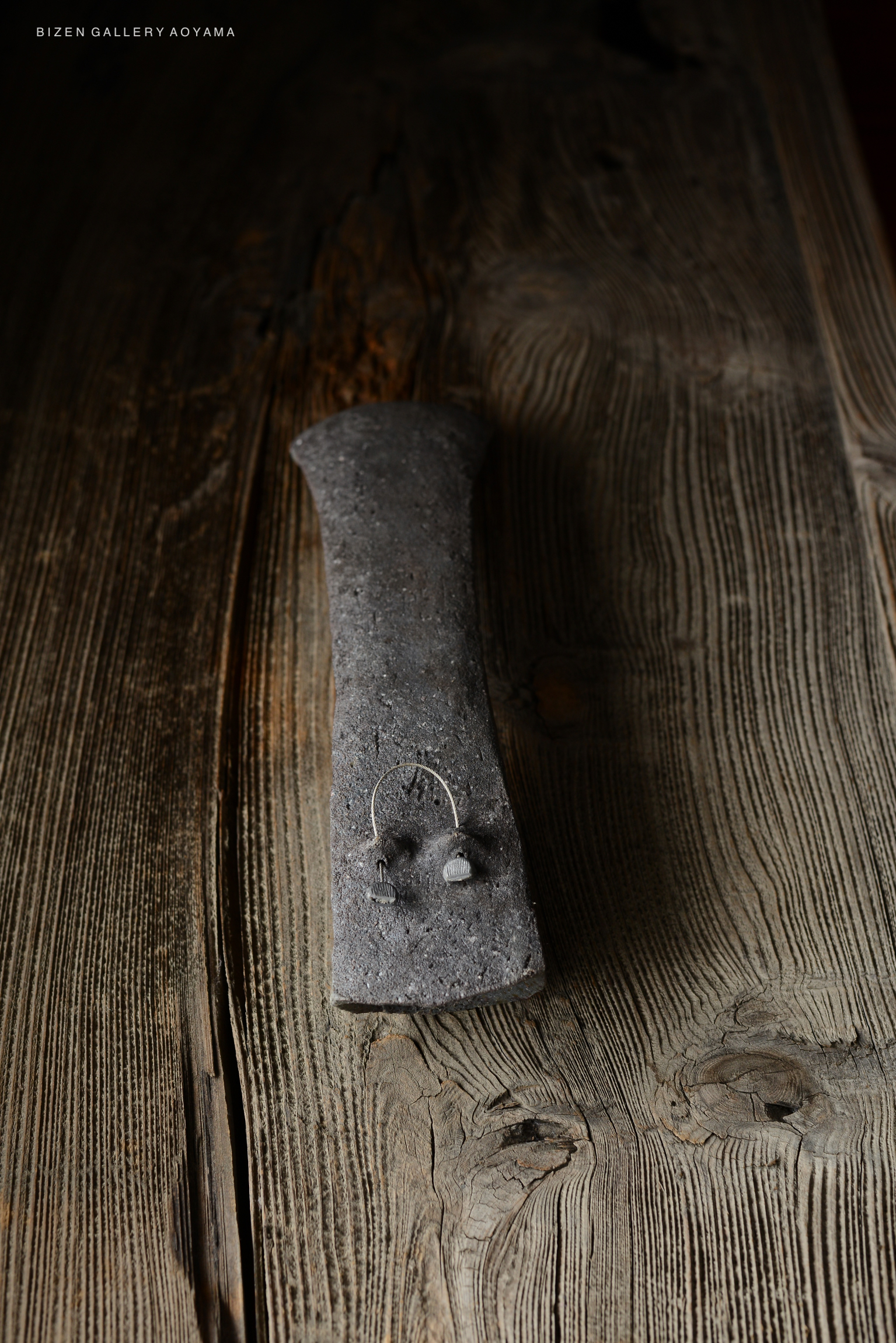 A close-up of a textured, dark ceramic piece resembling a traditional Japanese craft, resting on a wooden surface.