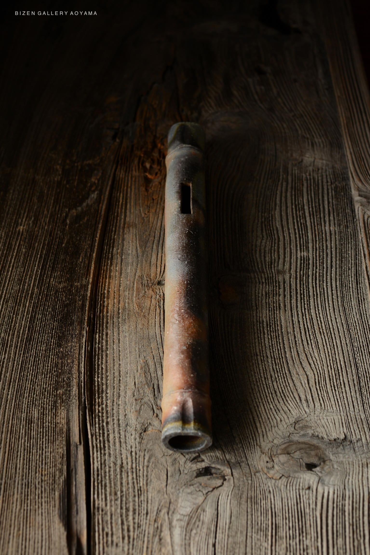 A close-up of a traditional Bizen pottery flute lying on a wooden surface, showcasing its natural textures and earthy colors.