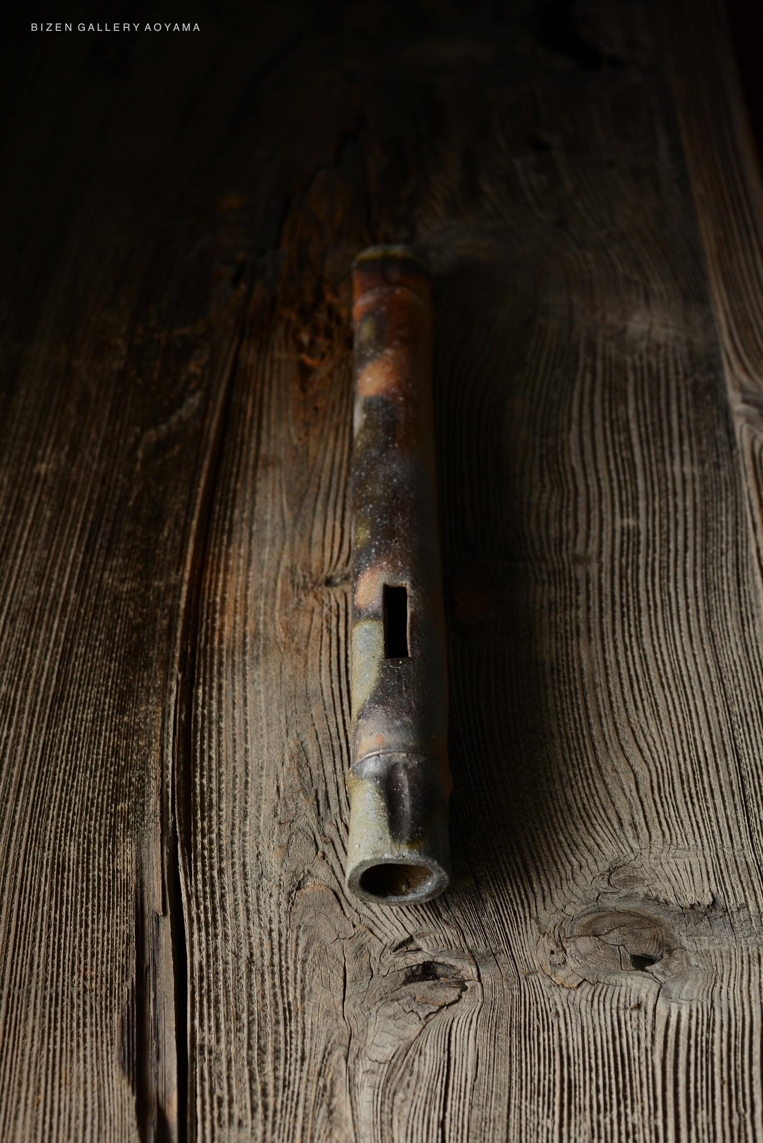 Close-up of a traditional Bizen pottery flute resting on textured wood.