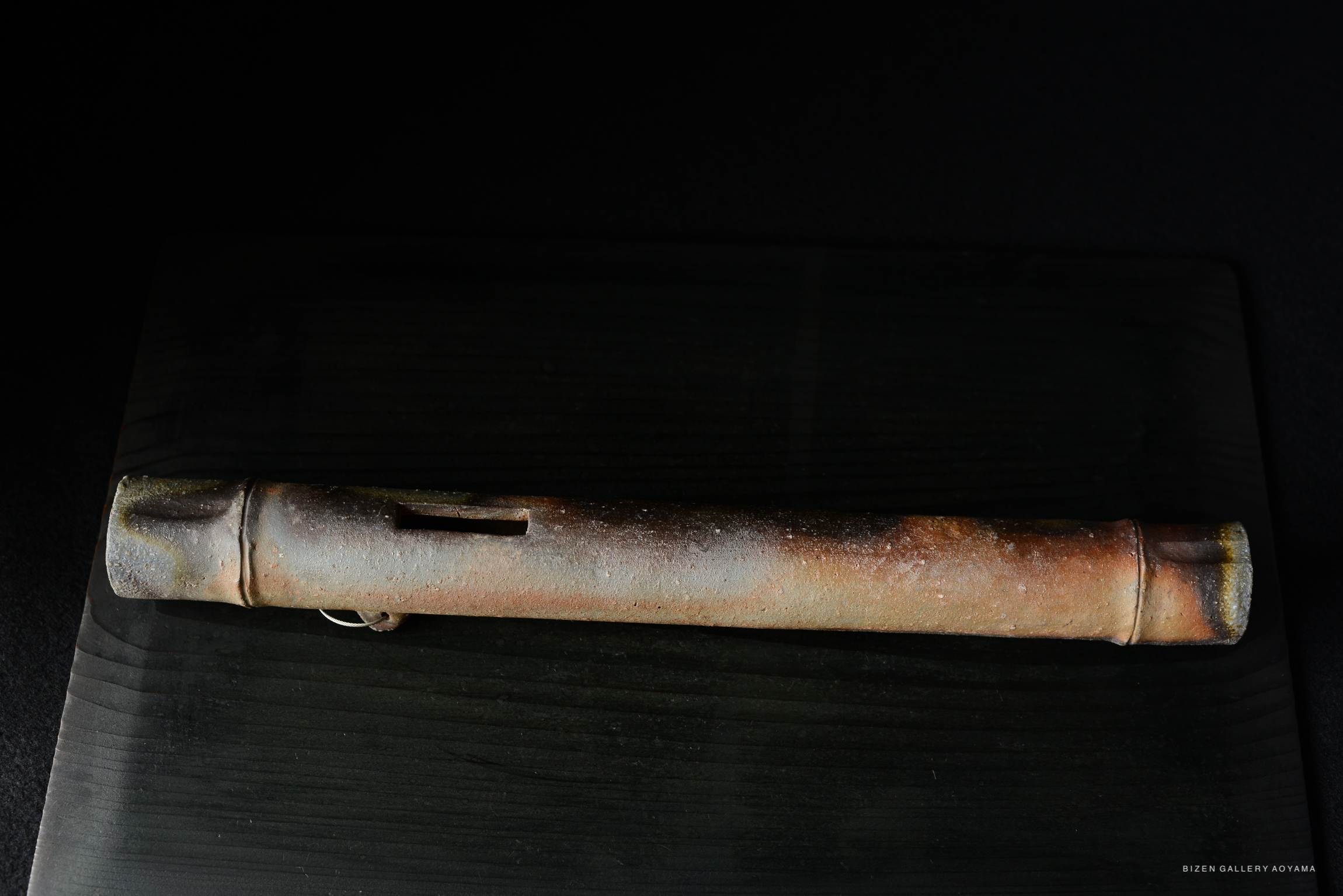 View of an elongated, weathered ceramic object resting on a dark wooden surface.