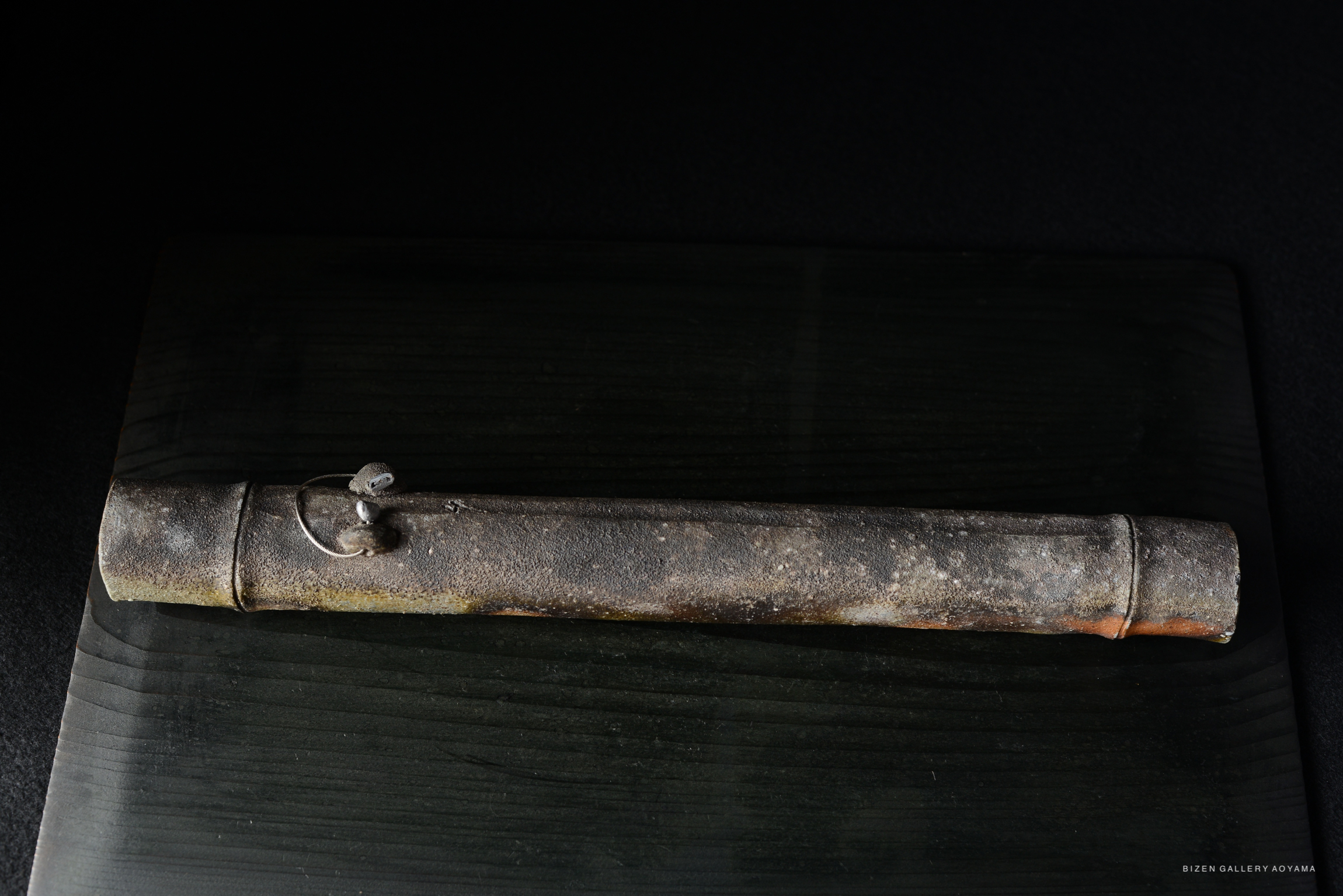 A close-up view of a textured, aged ceramic tube with a clasp, resting on a dark wooden surface.