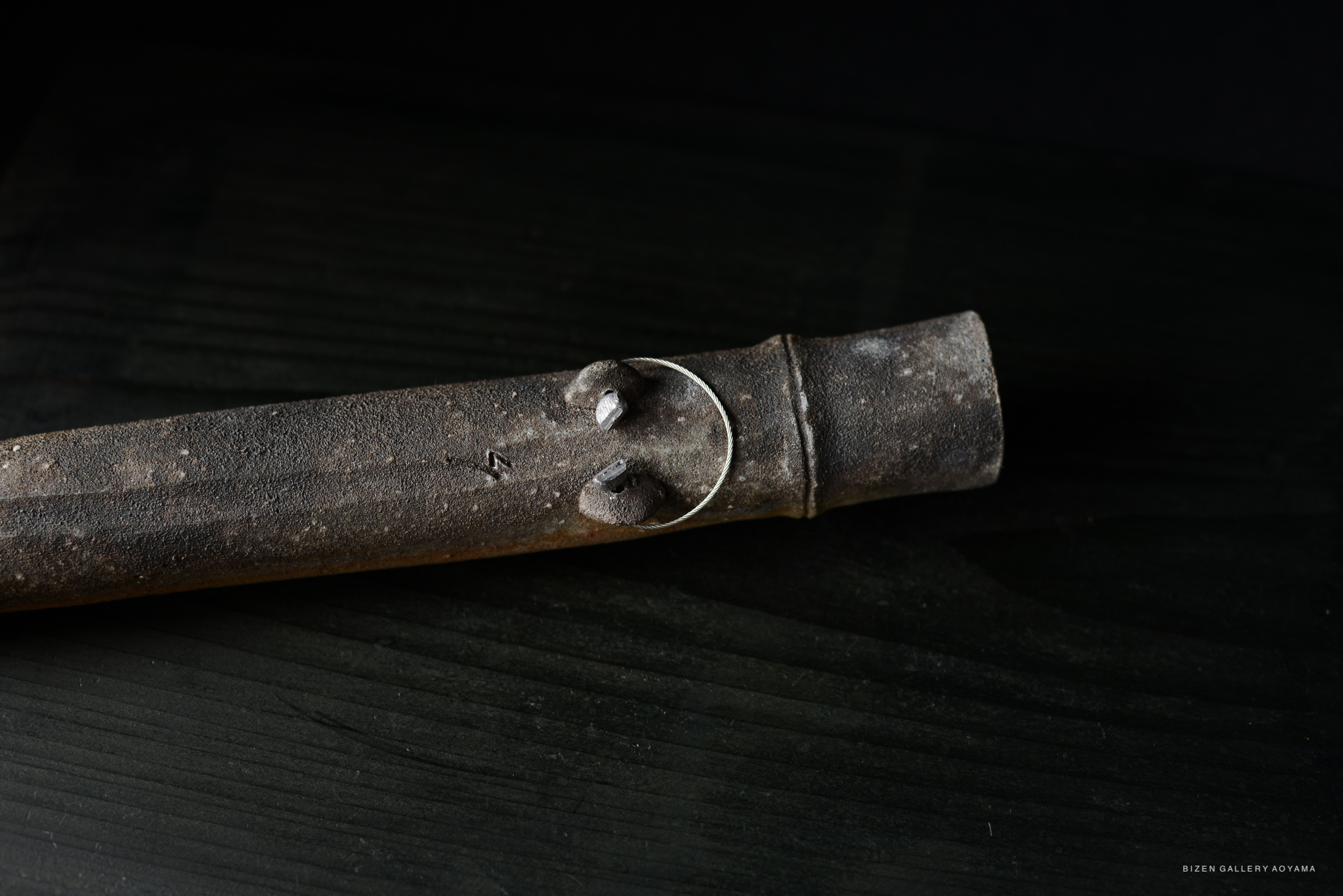 A close-up of a rustic, textured ceramic piece with a circular silver ring attached, resting on a dark wooden surface.