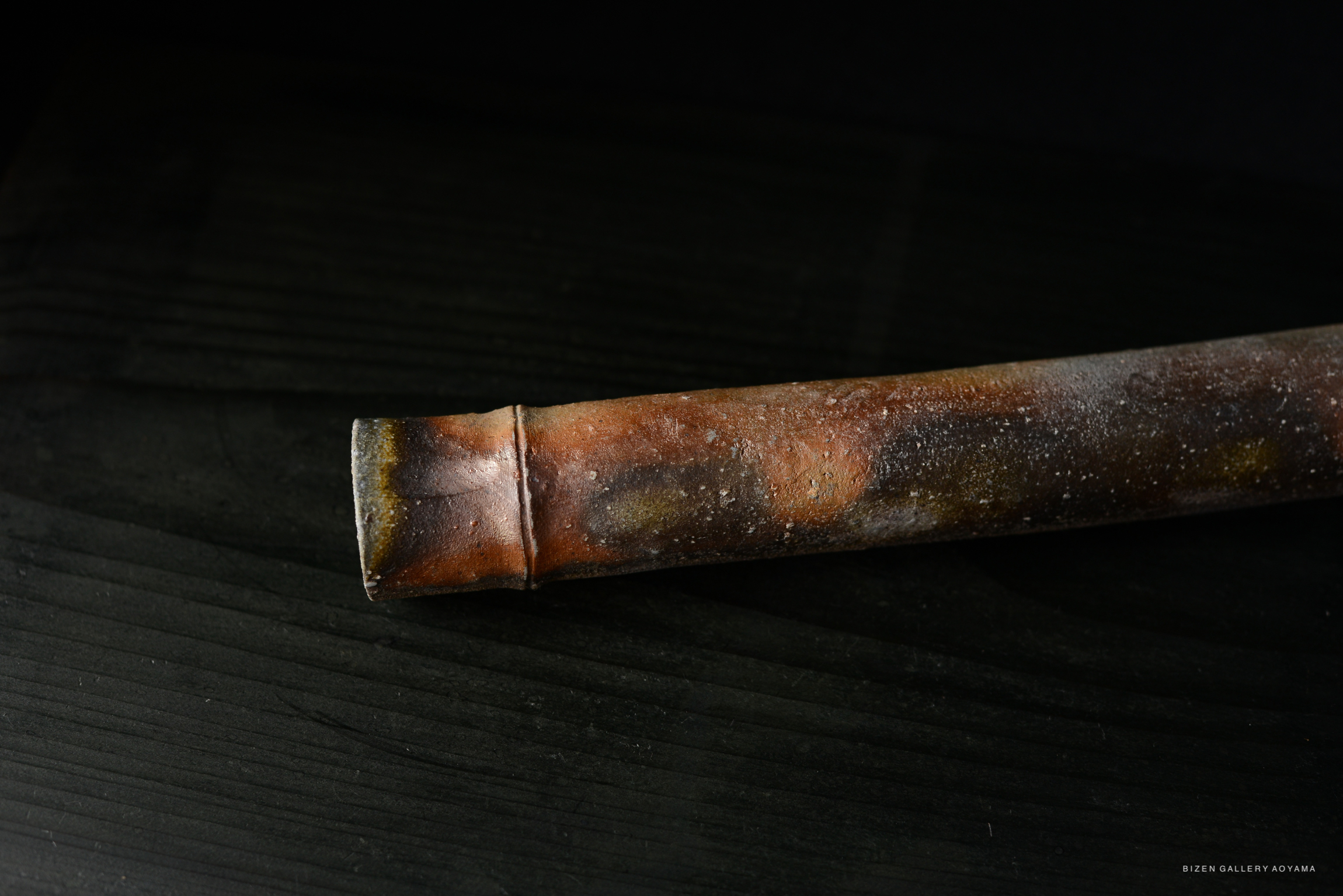 Close-up view of a rustic, textured wooden object with earthy tones, including browns and grays, resting on a dark surface.
