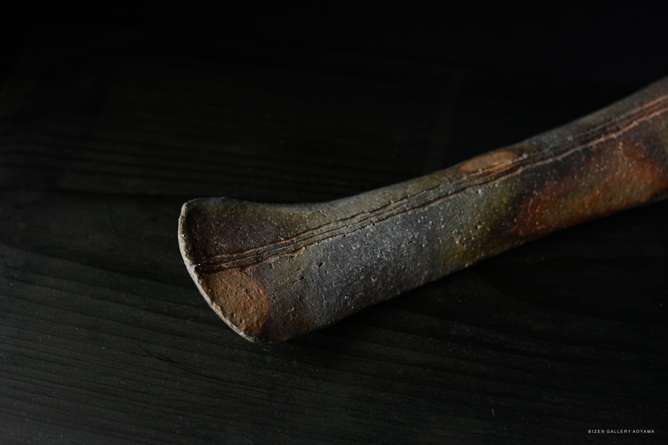 Close-up of a textured ceramic object with an elongated shape, showing earthy tones and a slightly worn surface.