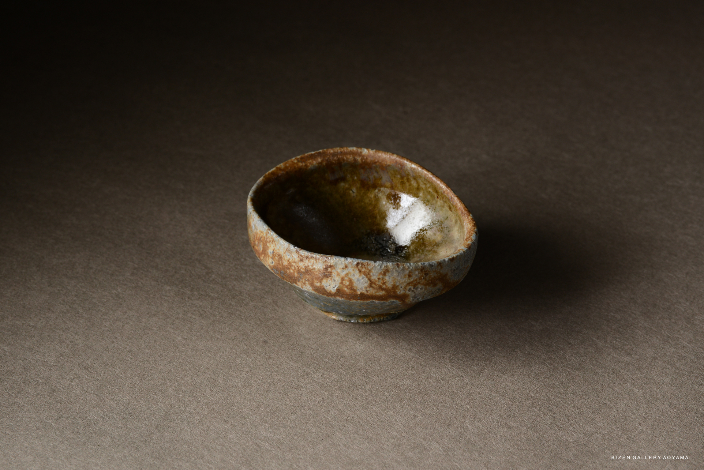 A small, rustic ceramic bowl with an irregular shape and a textured surface, featuring earthy tones and a glossy interior.