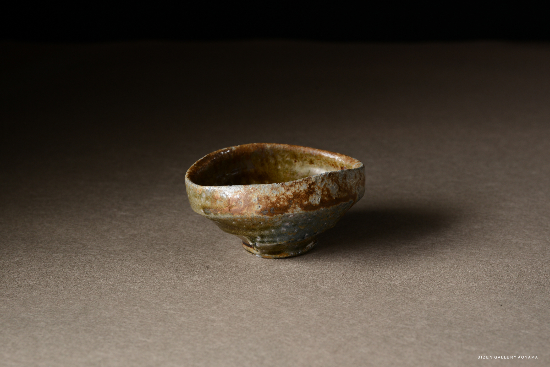 A close-up image of a rustic pottery bowl with a textured surface and earthy tones, displayed on a gray background.