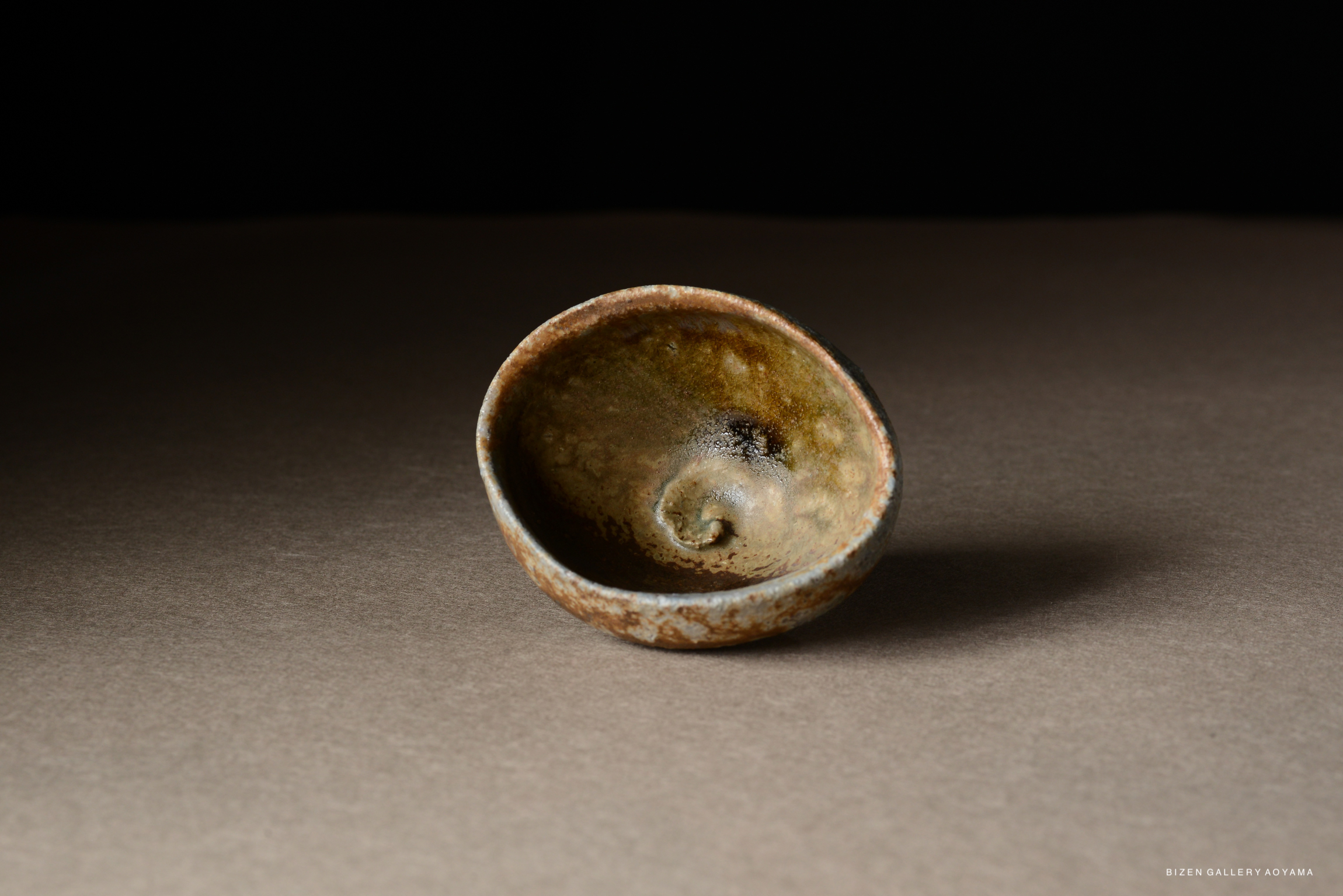 A close-up view of a handcrafted pottery bowl with a spiral design, placed on a neutral background.