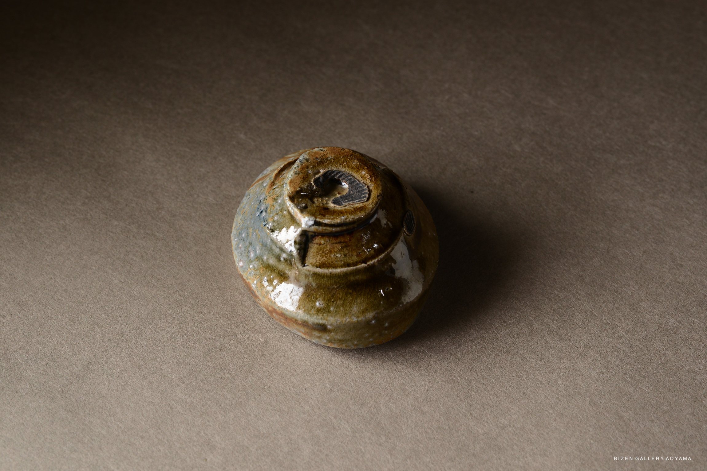 A small, round ceramic pot with a textured, multicolored glaze, placed on a neutral background.