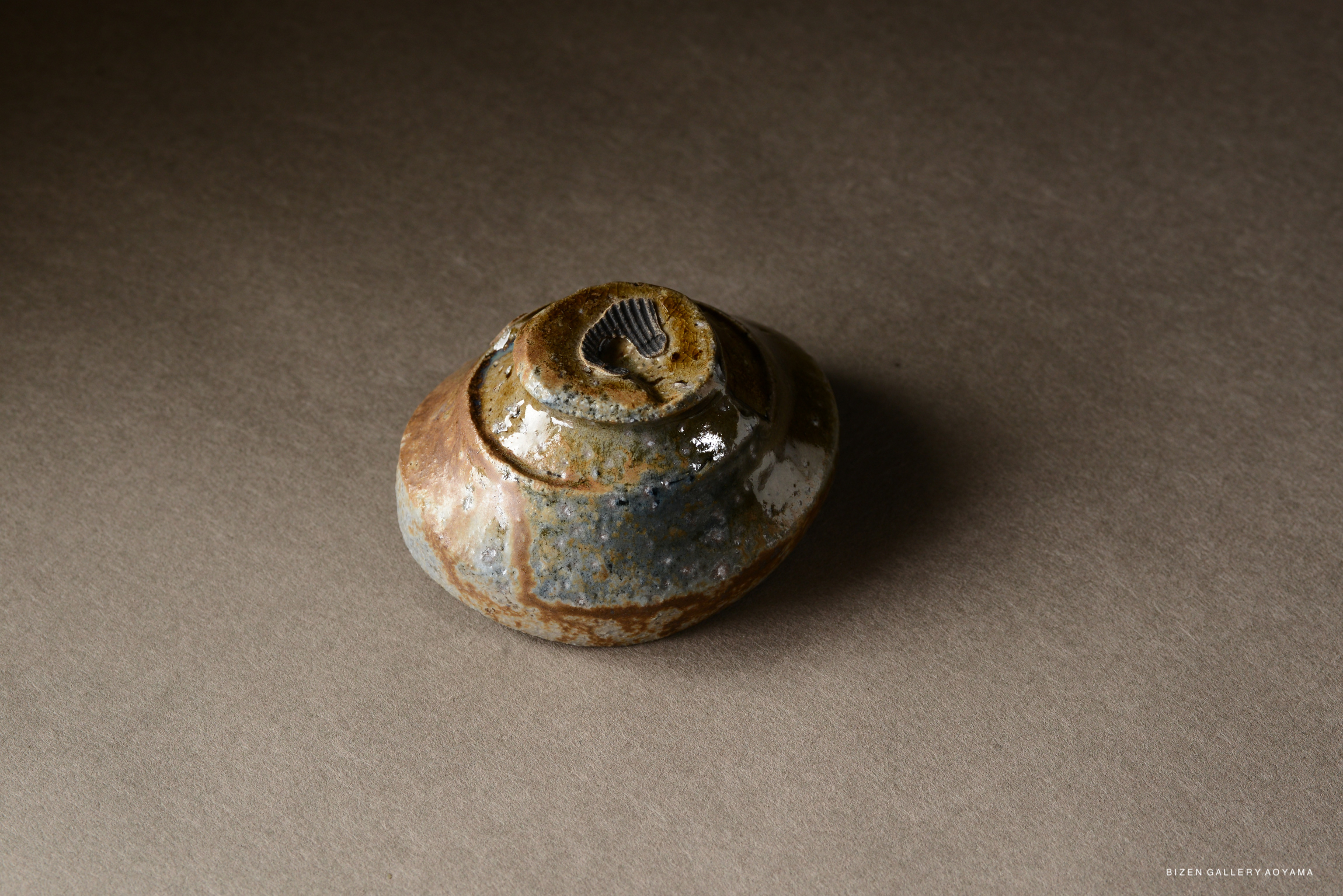 A unique Bizen pottery piece featuring a rounded shape with earthy, mottled glazes, resting on a neutral surface.