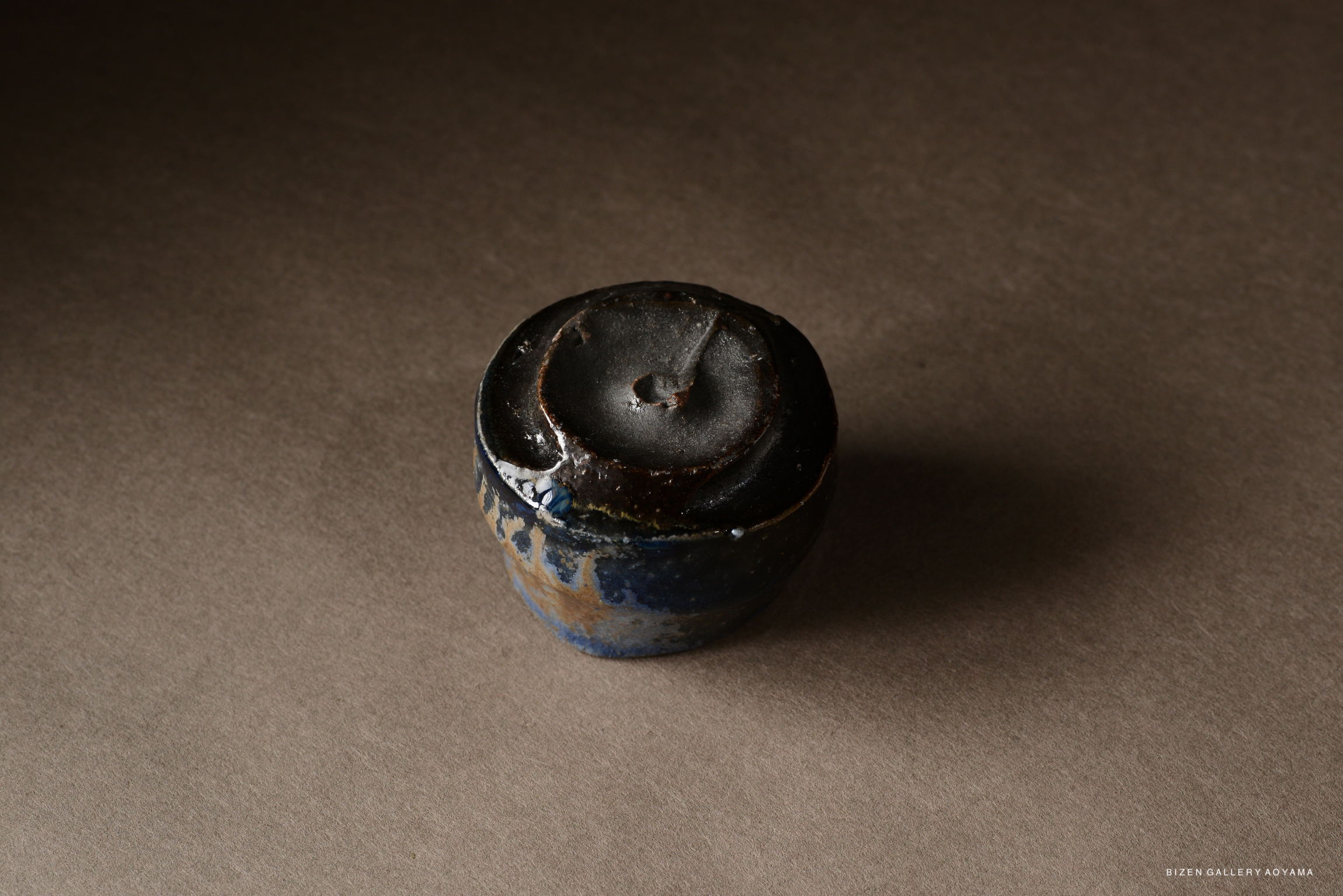 A small ceramic pot with a dark, glossy surface and a rounded top, resting on a neutral background.