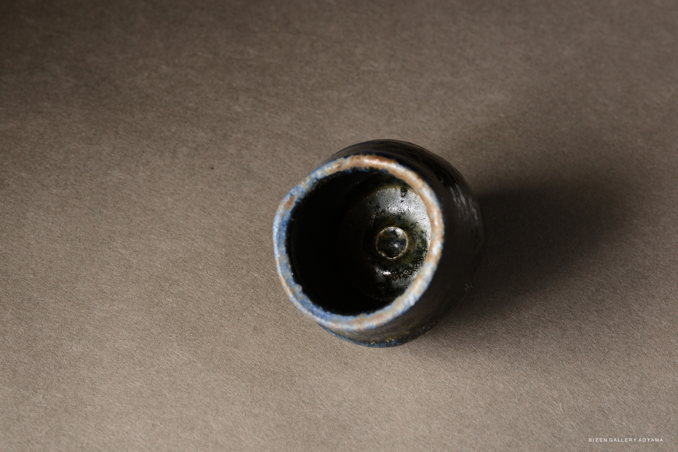 Top view of a small, round ceramic pot with a dark glaze and artistic imperfections, set against a neutral background.