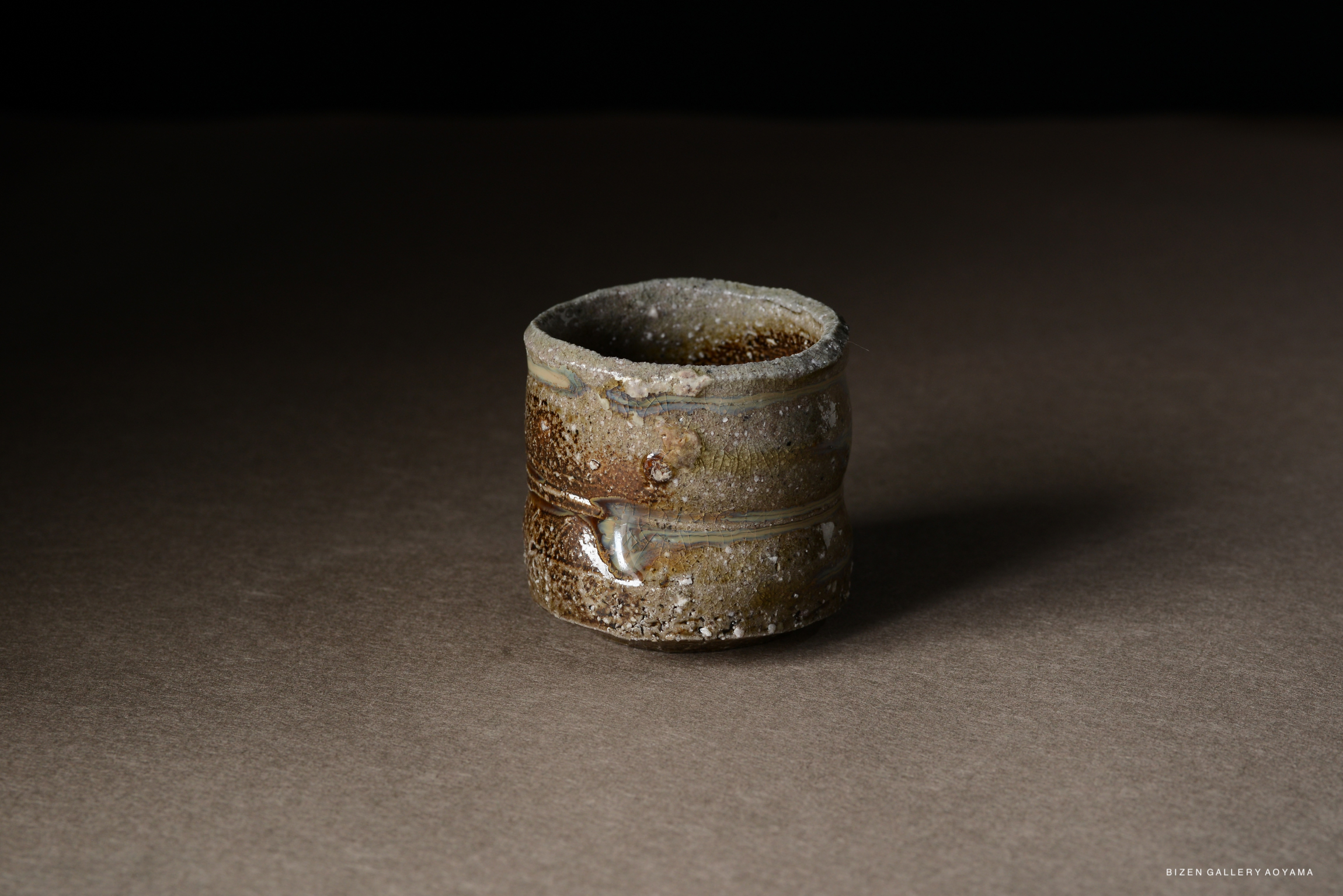 A rustic ceramic cup with a textured surface and earthy tones, displayed on a contrasting dark background.