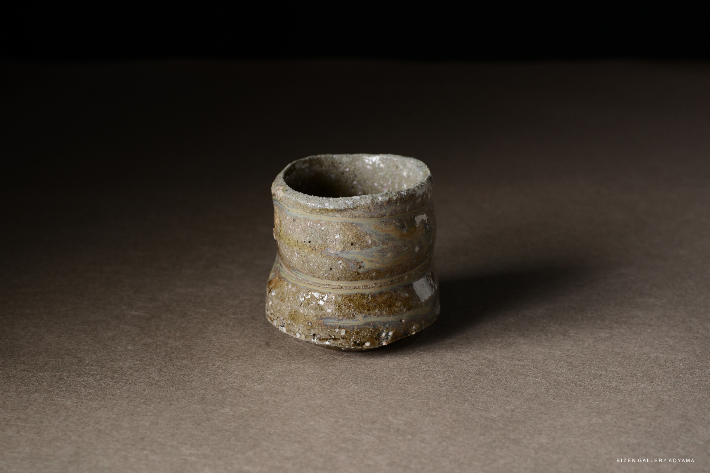 Close-up of a textured ceramic cup with earthy tones, featuring a slightly curved shape and a rough exterior surface.