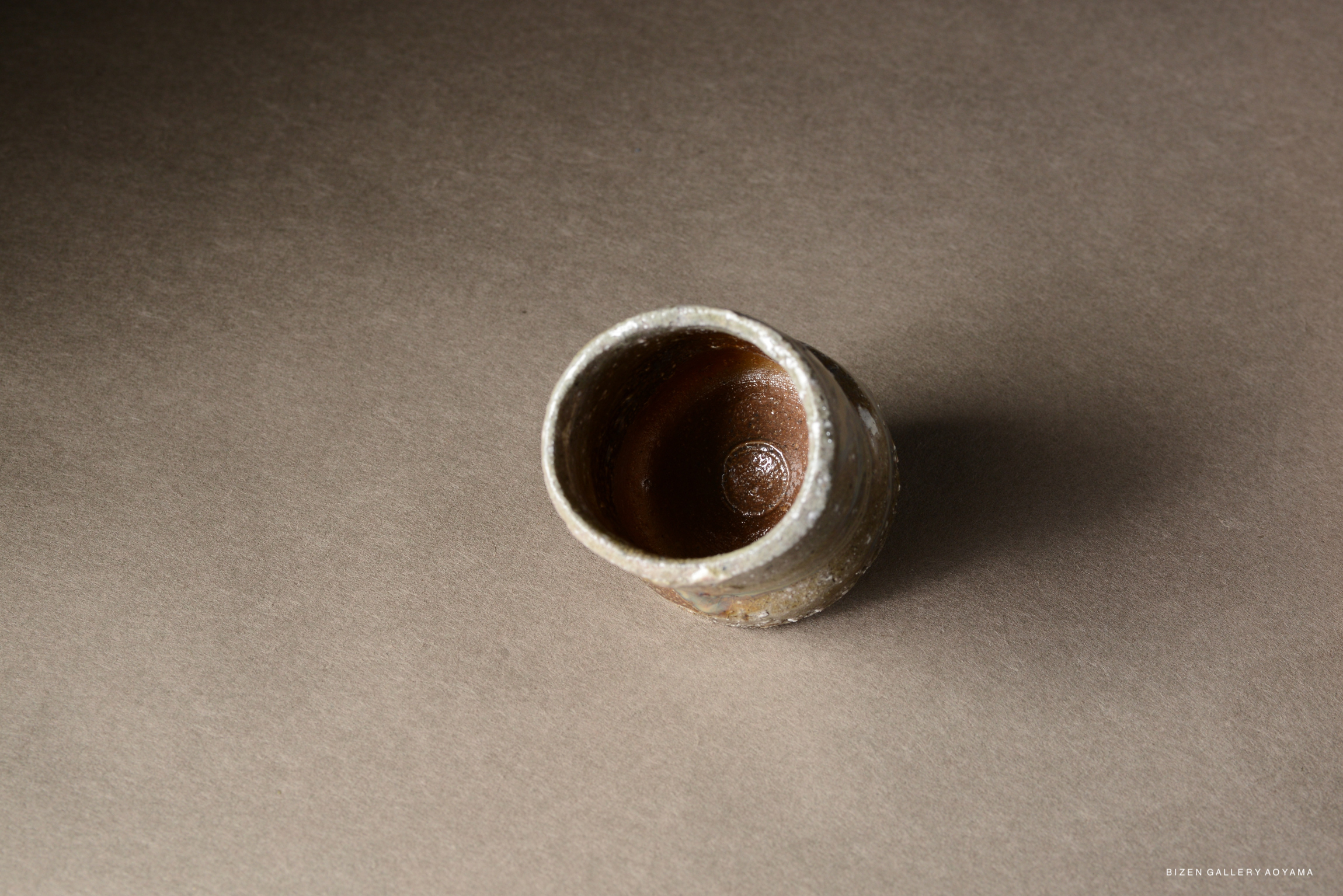 A small, rustic pottery vessel with a rounded shape, showing a textured surface and an earthy brown interior, placed on a neutral background.
