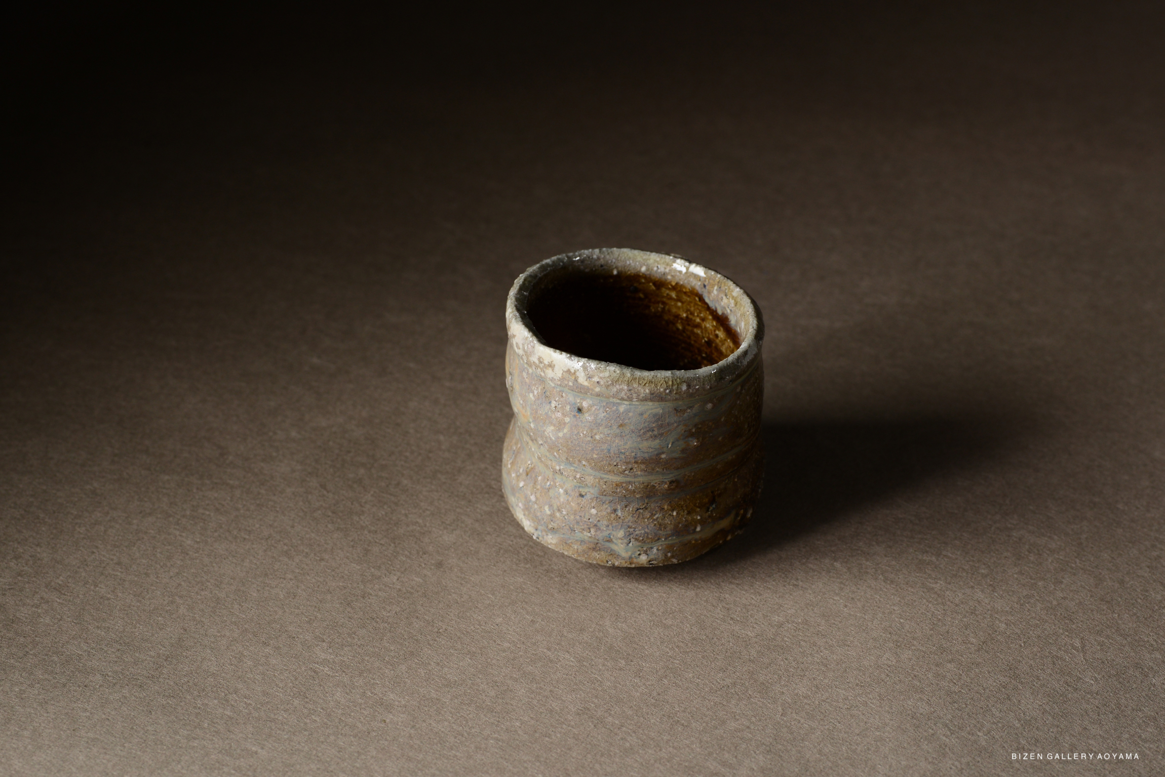 A rustic ceramic cup with a textured surface and earthy tones, placed on a dark background.